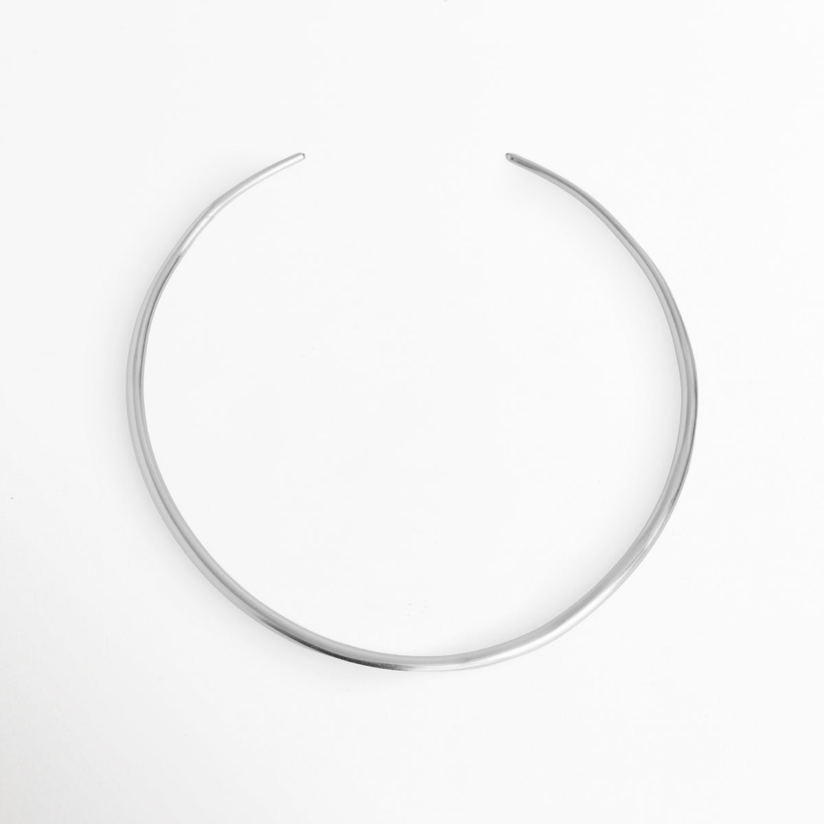 Collar Silver Cirella tipo choker rígido y abierto de 0.4 cm enchapado en oro blanco con pulido espejo, vista frontal circular sobre fondo blanco, Gargantilla rígida ajustada de cobre enchapado en oro blanco con diseño minimalista de aro abierto, Vista de frente de collar rígido tubular abierto en tono plata de estilo vanguardista y moderno, Collar tipo gargantilla rígida ajustable en oro blanco pulido sobre superficie clara.