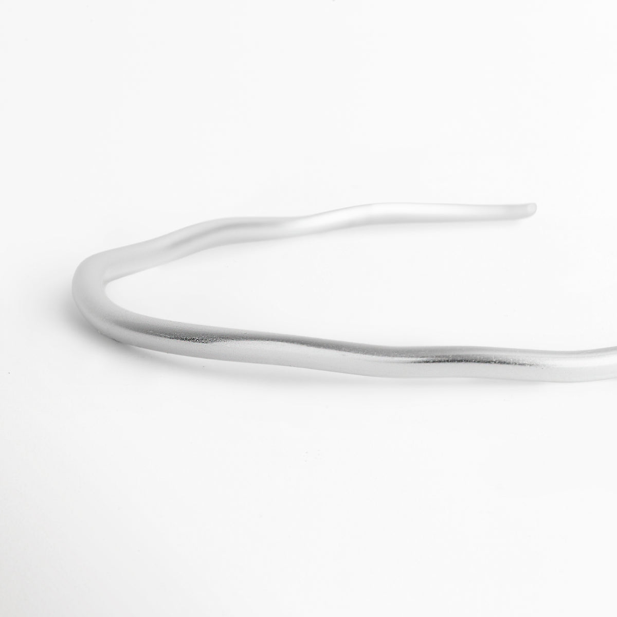 Vista de perfil en ángulo de la gargantilla Silver Cirella mostrando el grosor uniforme de 0.4 cm y la curvatura ergonómica, Detalle en perspectiva del acabado pulido en oro blanco del collar rígido abierto Toma de cerca de la superficie tubular lisa de la gargantilla ajustable de estilo contemporáneo, Vista lateral del collar choker Silver Cirella evidenciando su estructura metálica de acabado espejo.
