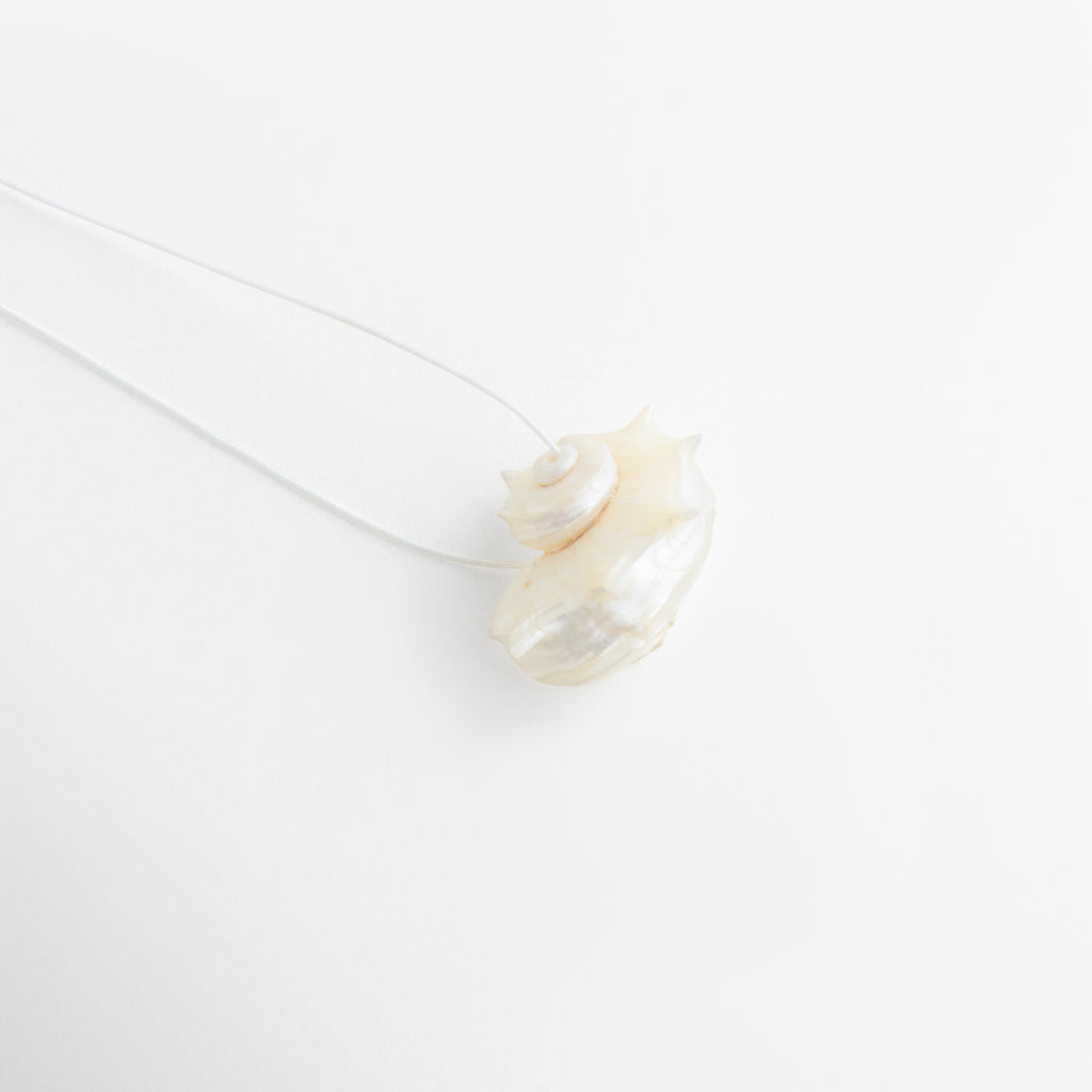 Detalle lateral del Collar Largo Oceana con acabado de caracola y diseño orgánico elegante, Vista cercana del colgante de caracola con textura natural y estilo sofisticado, Acercamiento del diseño del Collar Oceana con forma irregular inspirada en el mar, Detalle artístico del collar largo con colgante de caracola y acabado contemporáneo, Vista de perfil del dije del Collar Largo Oceana con esencia marina y toque exclusivo.