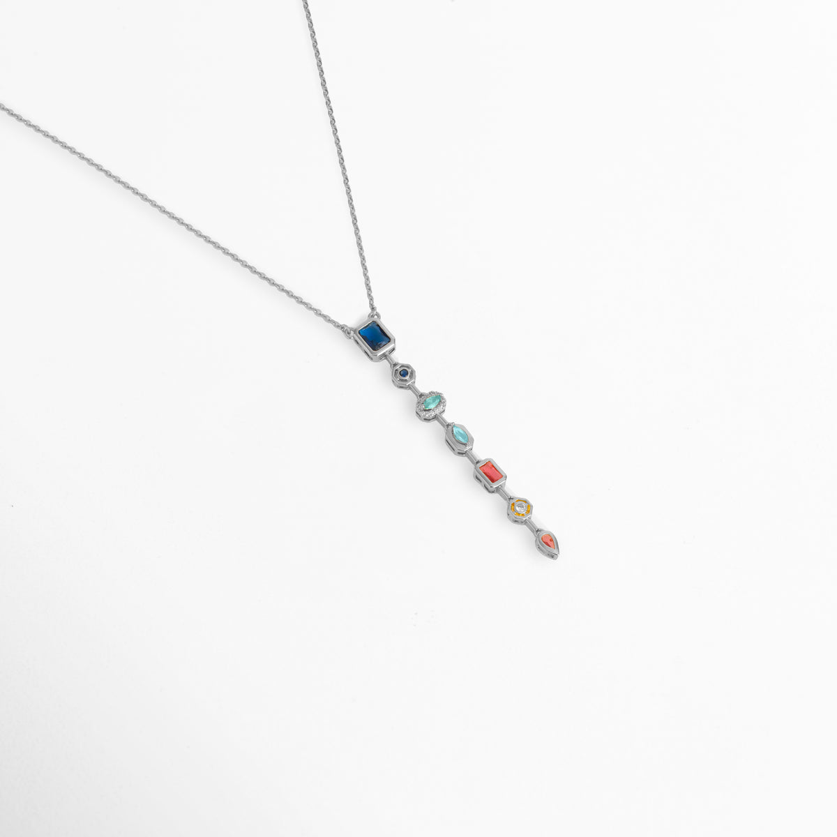 Toma en perspectiva del collar Silver Prisma mostrando cómo cuelga el dije multicolor sobre la cadena plateada de 40 cm, Vista de lado del collar plateado con colgante vertical de piedras de color en caída suave, Estilismo del Collar Silver Prisma en posición diagonal resaltando el contraste de tonos fríos y cálidos de las circonias, Muestra de la elegancia y movimiento del dije alargado multicolor enchapado en oro blanco.