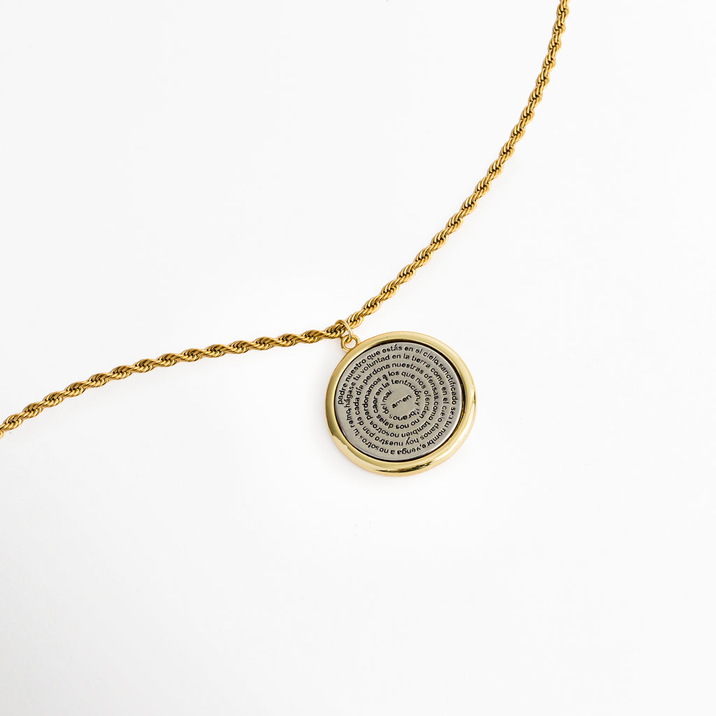 Vista del reverso del dije del Collar Padre Nuestro Bitono mostrando el grabado con motivo de cruz en acabado bitono, Acercamiento a la parte posterior de la medalla con diseño de cruz labrada en tono plata y borde dorado, Toma en detalle del reverso del dije de 3.2 cm sostenido por la cadena de cordón enchapada en oro, Muestra de la textura y acabado posterior de la medalla devocional bitono.   