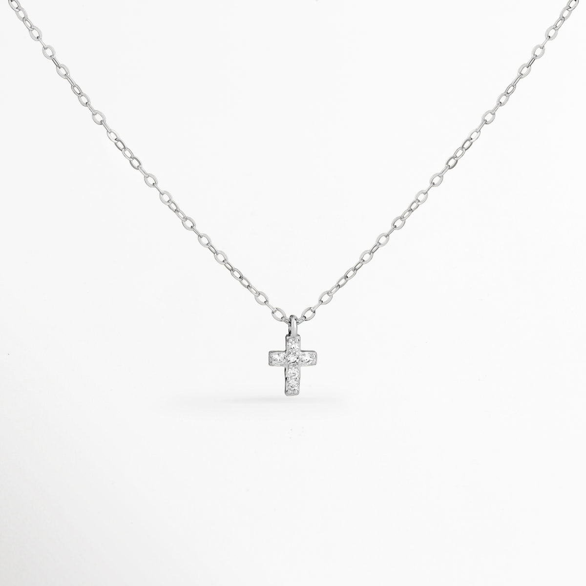 Collar Silver Gloria de plata ley 925 enchapado en oro blanco 14K con dije mini de cruz cuajado de circonias, vista de frente sobre fondo blanco, Vista frontal de collar plateado con dije de cruz pequeña de 0.8 cm de largo con pavé de circonias brillantes, Plano general de collar fino de plata ley 925 enchapado en oro blanco 14K con dije de cruz diminuta sobre cadena de 41 cm, Collar Silver Gloria destacando los destellos de las circonias transparentes 
