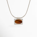 Collar Tigra con colgante rectangular de piedra tipo Ojo de Tigre y cadena con acabado en Oro Blanco sobre fondo blanco, Vista frontal del Collar Tigra con dije de piedra tipo Ojo de Tigre y cadena de cobre con recubrimiento en Oro Blanco, Collar Tigra con colgante de piedra Ojo de Tigre en diseño minimalista y acabado en Oro Blanco, Collar de mujer Tigra con dije rectangular de piedra Ojo de Tigre y cadena fina en acabado Oro Blanco, Collar Tigra elaborado en cobre con recubrimiento en Oro Blanco