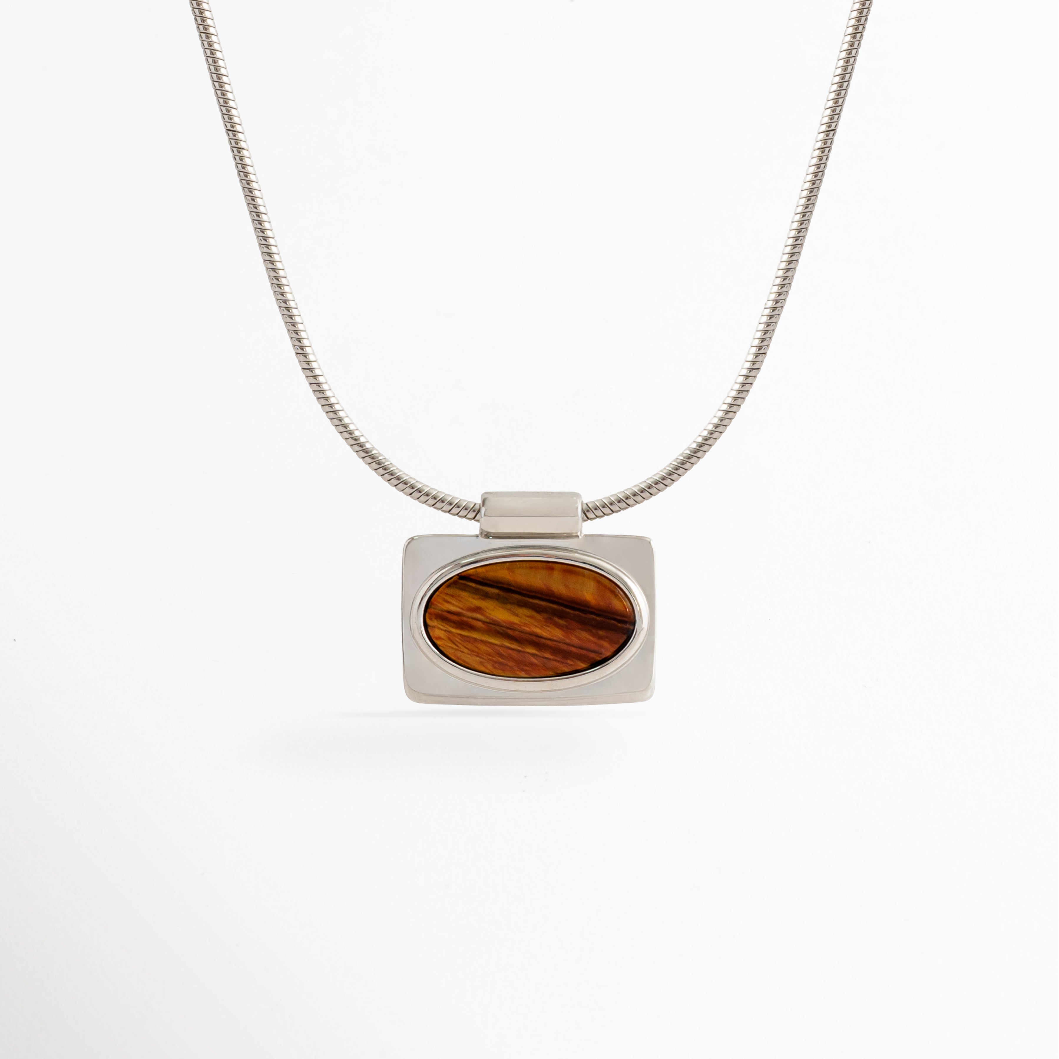 Collar Tigra con colgante rectangular de piedra tipo Ojo de Tigre y cadena con acabado en Oro Blanco sobre fondo blanco, Vista frontal del Collar Tigra con dije de piedra tipo Ojo de Tigre y cadena de cobre con recubrimiento en Oro Blanco, Collar Tigra con colgante de piedra Ojo de Tigre en diseño minimalista y acabado en Oro Blanco, Collar de mujer Tigra con dije rectangular de piedra Ojo de Tigre y cadena fina en acabado Oro Blanco, Collar Tigra elaborado en cobre con recubrimiento en Oro Blanco