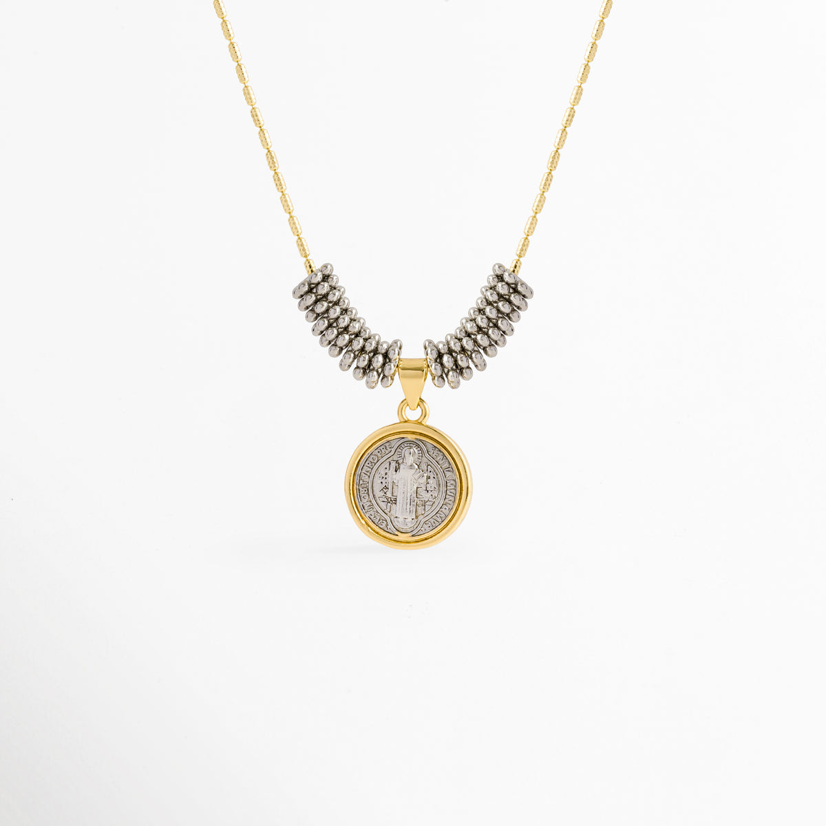 Collar Bitono San Benito enchapado en oro y oro blanco con medalla circular de San Benito y cuentas plateadas, vista de frente sobre fondo blanco, Vista frontal de collar religioso bitono con dije de medalla de San Benito de 2.2 cm flanqueado por cuentas plateadas tubulares, Plano general de collar protector bitono con dije circular de San Benito en relieve sobre cadena fina dorada con adorno de cuentas plata, Collar Bitono San Benito de cobre enchapado en oro
