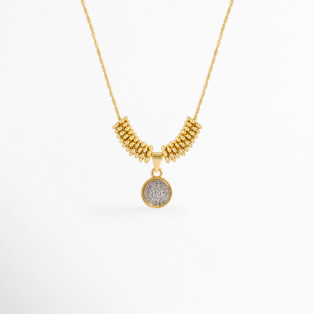 Collar Golden San Benito enchapado en oro con dije circular plateado de la medalla de San Benito y cuentas doradas, vista de frente sobre fondo blanco, Vista frontal de collar religioso con dije de medalla de San Benito de 1.7 cm flanqueado por cuentas doradas tubulares, Plano general de collar protector con dije circular de San Benito en relieve sobre cadena fina con adorno de cuentas, Collar Golden San Benito de cobre enchapado en oro mostrando el contraste