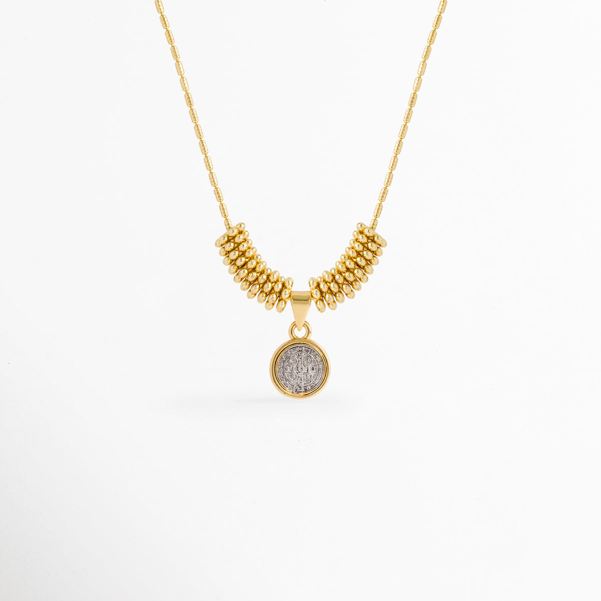 Collar Golden San Benito enchapado en oro con dije circular plateado de la medalla de San Benito y cuentas doradas, vista de frente sobre fondo blanco, Vista frontal de collar religioso con dije de medalla de San Benito de 1.7 cm flanqueado por cuentas doradas tubulares, Plano general de collar protector con dije circular de San Benito en relieve sobre cadena fina con adorno de cuentas, Collar Golden San Benito de cobre enchapado en oro mostrando el contraste