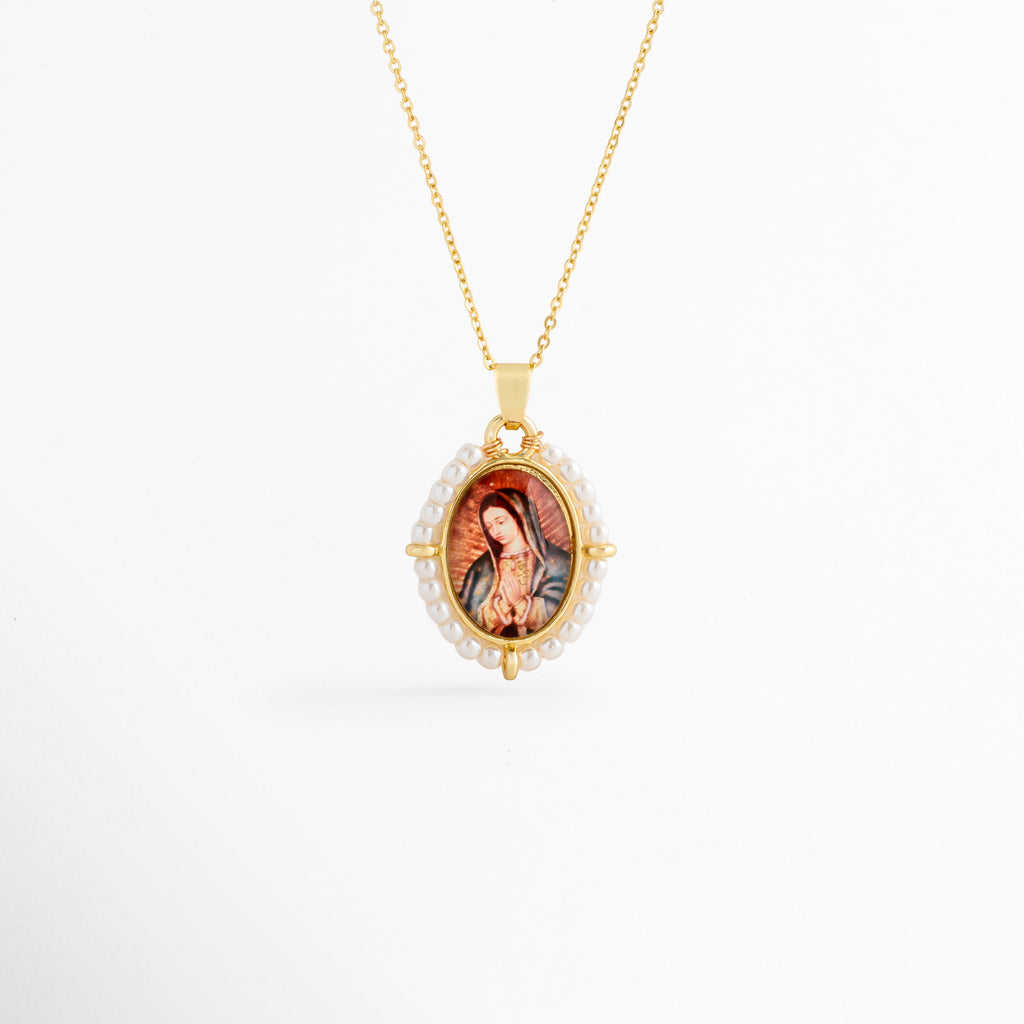 Collar Medallón Imagen Virgen de cobre con recubrimiento en oro y perlas de agua dulce, vista frontal, Collar dorado con medallón de la Virgen enmarcado por perlas de agua dulce, vista frontal sobre fondo blanco, Vista frontal del Collar Medallón Imagen Virgen con cadena dorada y dije ovalado, Collar religioso con imagen de la Virgen y borde de perlas de agua dulce, vista frontal, Collar Medallón Imagen Virgen con dije ovalado de 3.2 cm y acabado en oro.