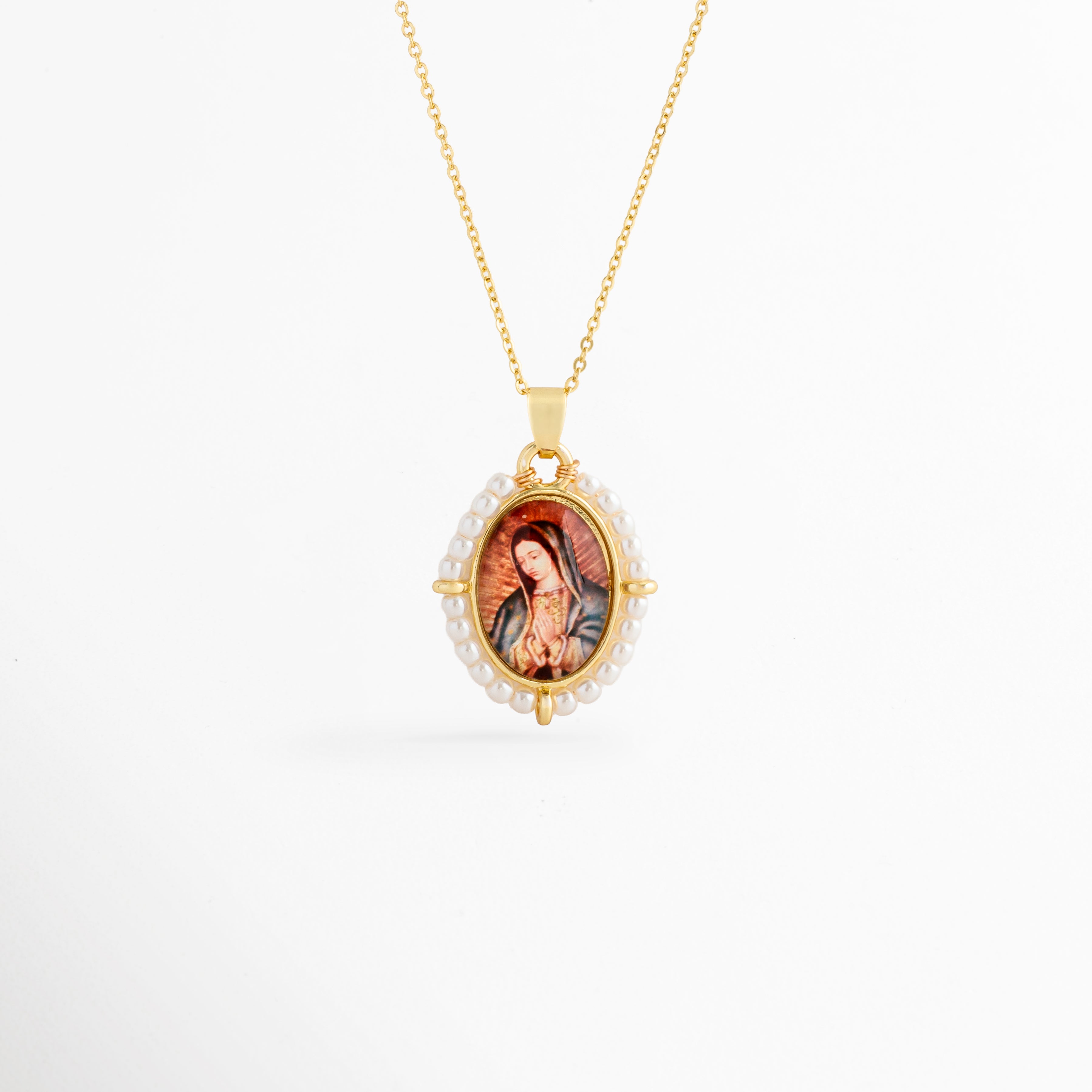 Collar Medallón Imagen Virgen de cobre con recubrimiento en oro y perlas de agua dulce, vista frontal, Collar dorado con medallón de la Virgen enmarcado por perlas de agua dulce, vista frontal sobre fondo blanco, Vista frontal del Collar Medallón Imagen Virgen con cadena dorada y dije ovalado, Collar religioso con imagen de la Virgen y borde de perlas de agua dulce, vista frontal, Collar Medallón Imagen Virgen con dije ovalado de 3.2 cm y acabado en oro.