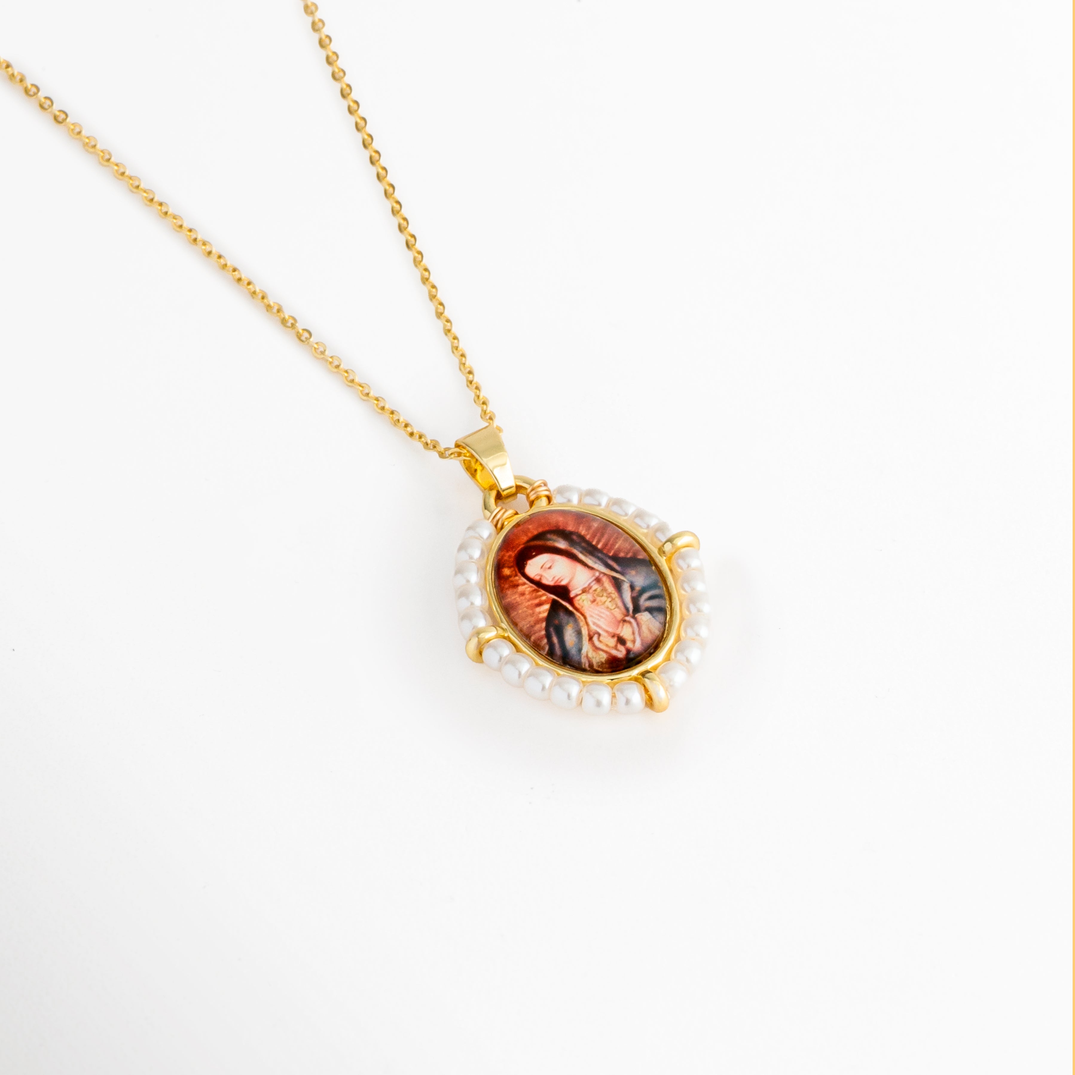 Acercamiento del medallón con imagen de la Virgen y perlas de agua dulce del Collar Medallón Imagen Virgen, Detalle del dije ovalado con imagen religiosa y acabado dorado, Primer plano del medallón de la Virgen enmarcado por perlas de agua dulce, Vista cercana del Collar Medallón Imagen Virgen que resalta los detalles del dije, Detalle del medallón ovalado con imagen de la Virgen y acabado en oro.