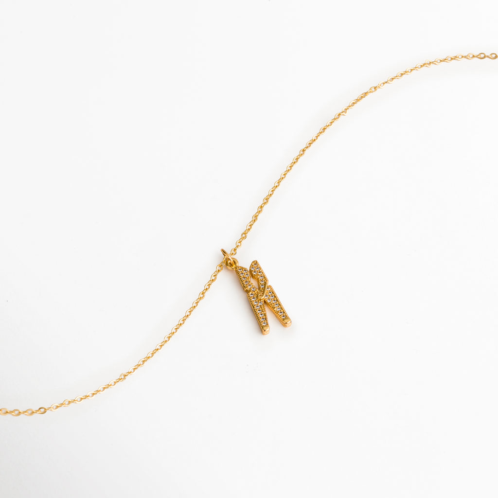 Vista extendida de la cadena fina enchapada en oro 18K con el dije de pinza de ropa reposando en curva suave, Toma aérea del Collar Grapa mostrando la fluidez de la cadena de 40 cm y el dije articulado con circonias, Muestra del brillo dorado y la integración del reasa del dije sobre la cadena delgada, Acercamiento al dije de gancho de ropa con pedrería deslizándose sobre la cadena dorada.