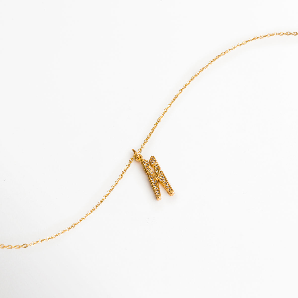 Vista extendida de la cadena fina enchapada en oro 18K con el dije de pinza de ropa reposando en curva suave, Toma aérea del Collar Grapa mostrando la fluidez de la cadena de 40 cm y el dije articulado con circonias, Muestra del brillo dorado y la integración del reasa del dije sobre la cadena delgada, Acercamiento al dije de gancho de ropa con pedrería deslizándose sobre la cadena dorada.