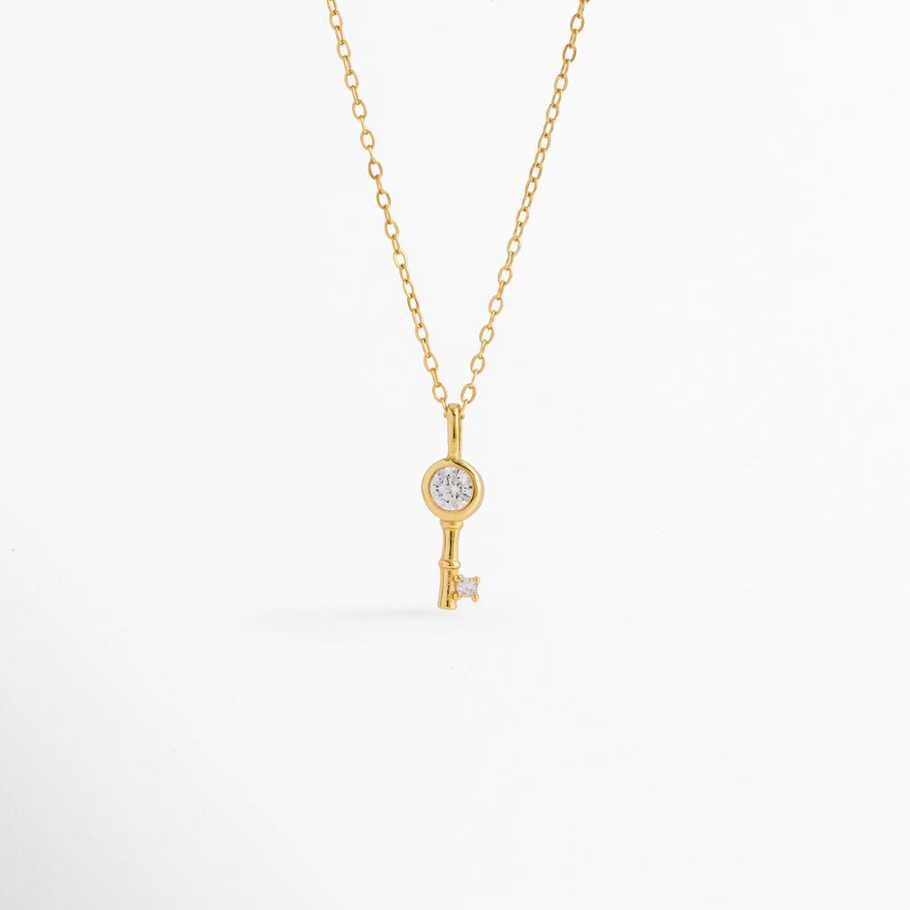 Collar Golden Kael de plata ley 925 enchapado en oro 14K con dije de llave minimalista y circonia central incrustada, vista de frente sobre fondo blanco, Vista frontal de collar dorado con dije de llave de 1.6 cm con pedrería brillante engastada en el cabezal y la punta, Plano general de collar fino de plata ley 925 enchapado en oro 14K con dije de llave delicada sobre cadena de 45 cm, Collar Golden Kael destacando los destellos de las circonias transparentes
