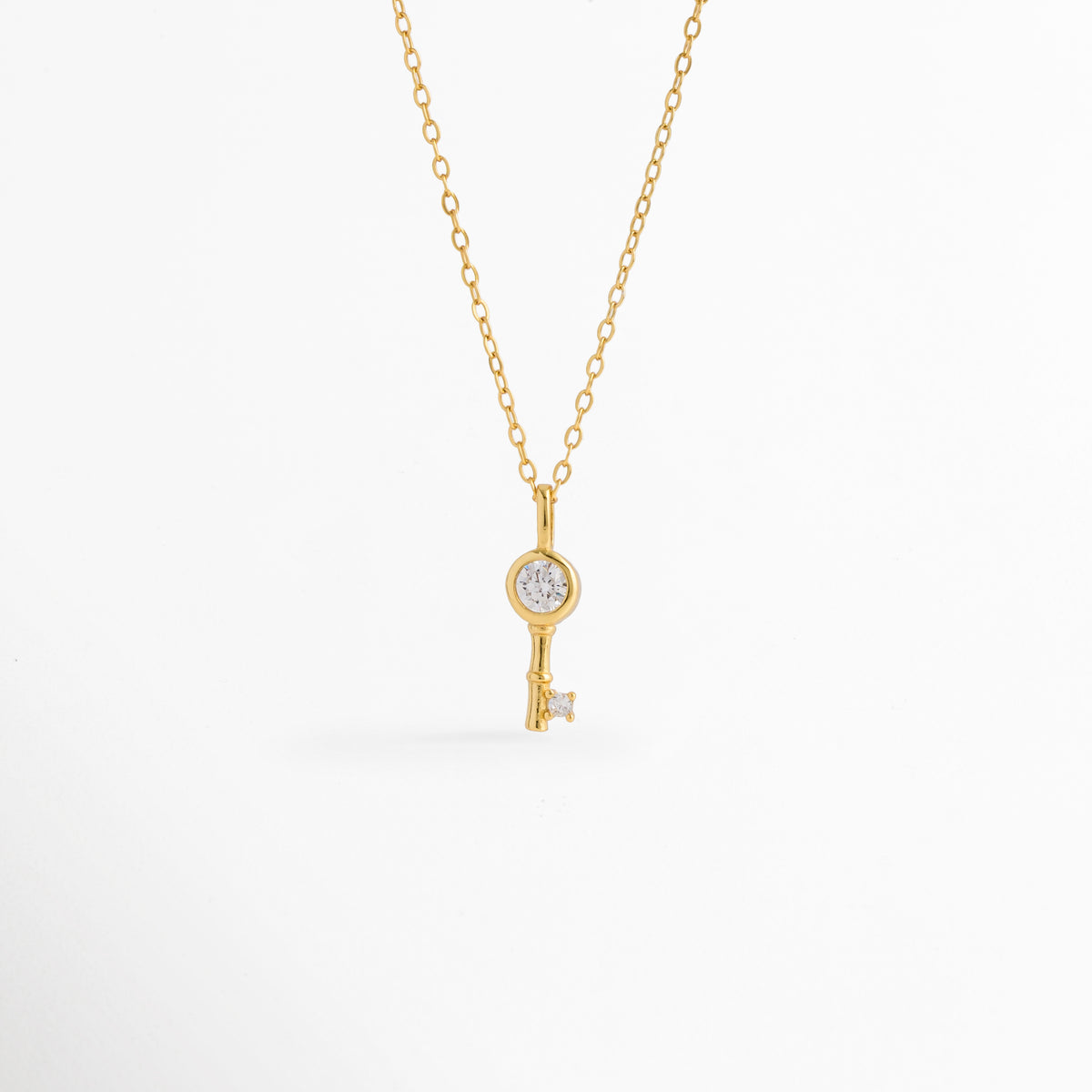 Collar Golden Kael de plata ley 925 enchapado en oro 14K con dije de llave minimalista y circonia central incrustada, vista de frente sobre fondo blanco, Vista frontal de collar dorado con dije de llave de 1.6 cm con pedrería brillante engastada en el cabezal y la punta, Plano general de collar fino de plata ley 925 enchapado en oro 14K con dije de llave delicada sobre cadena de 45 cm, Collar Golden Kael destacando los destellos de las circonias transparentes