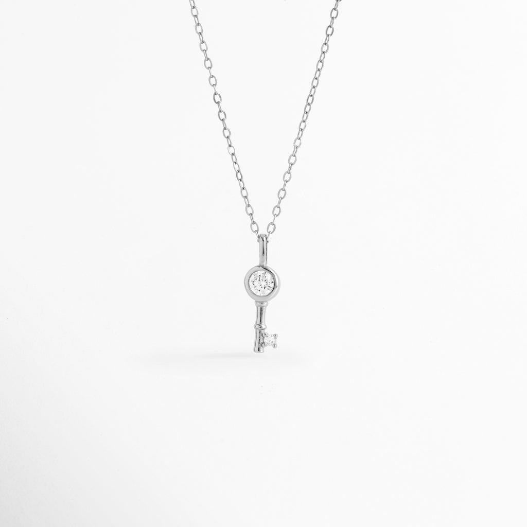 Collar Silver Kael de plata ley 925 enchapado en oro blanco 14K con dije de llave minimalista y circonia central incrustada, vista de frente sobre fondo blanco, Vista frontal de collar plateado con dije de llave de 1.6 cm con pedrería brillante engastada en el cabezal y la punta, Plano general de collar fino de plata ley 925 enchapado en oro blanco 14K con dije de llave delicada sobre cadena de 45 cm, Collar Silver Kael destacando los destellos de las circonias