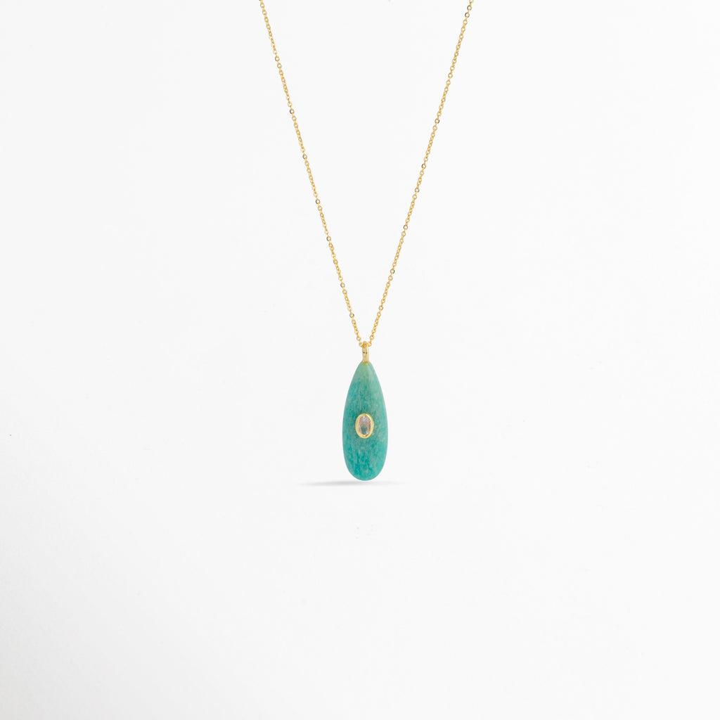 Collar Cuarzo Jade de cobre enchapado en oro con dije de piedra natural verde turquesa en forma de gota alargada e incrustación central cristalina, vista frontal sobre fondo blanco, Vista de frente de collar dorado con dije de cuarzo tono verde jade de 4 cm de largo y pequeño cristal ovalado incrustado al centro,  Plano general de collar fino con dije orgánico en forma de lágrima en piedra natural tono jade sobre fondo neutro.