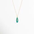 Collar Cuarzo Jade de cobre enchapado en oro con dije de piedra natural verde turquesa en forma de gota alargada e incrustación central cristalina, vista frontal sobre fondo blanco, Vista de frente de collar dorado con dije de cuarzo tono verde jade de 4 cm de largo y pequeño cristal ovalado incrustado al centro,  Plano general de collar fino con dije orgánico en forma de lágrima en piedra natural tono jade sobre fondo neutro.
