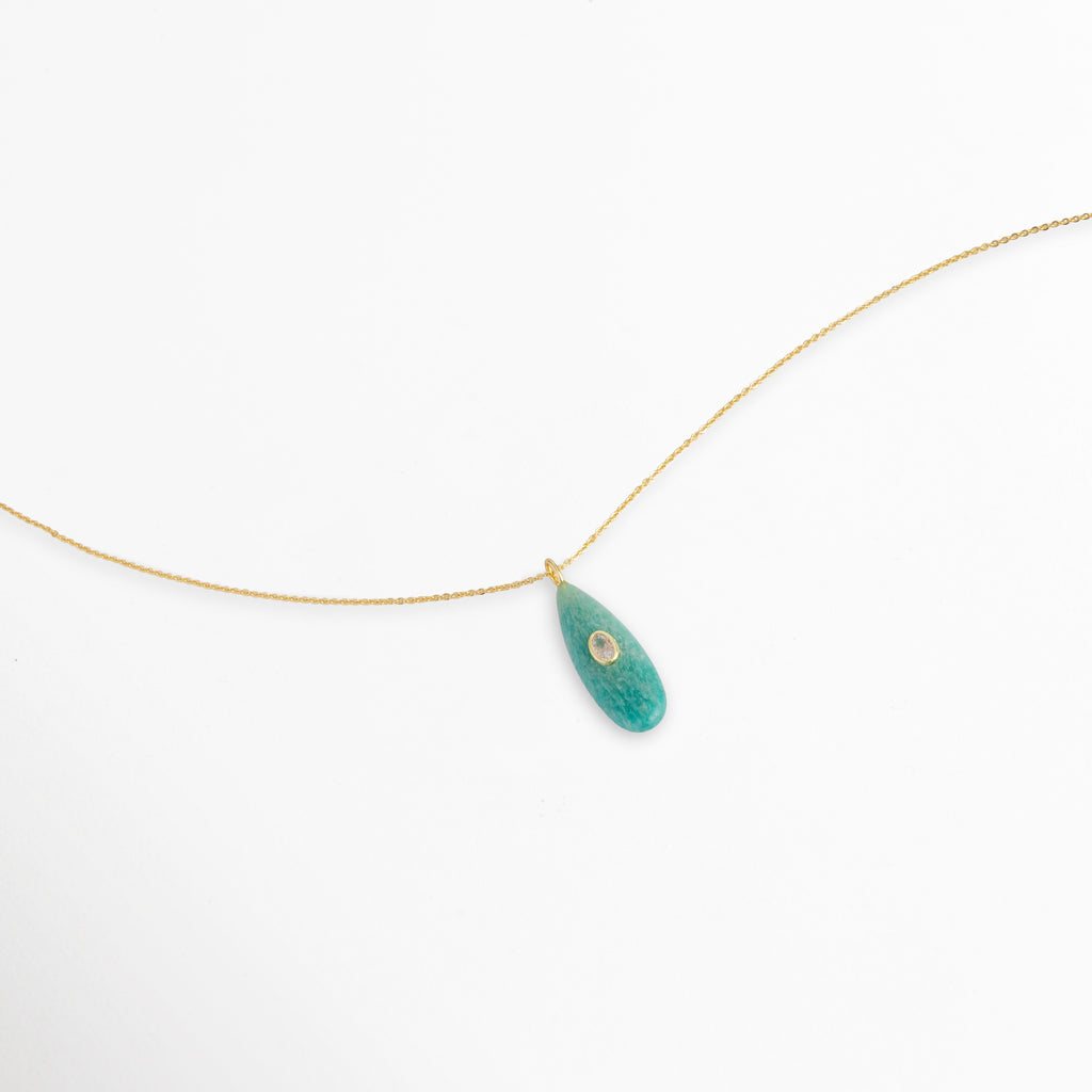 Vista aérea en curva suave del Collar Cuarzo Jade con el dije de gota verde jade reposando sobre fondo blanco, Toma extendida de la fina cadena dorada mostrando la soltura y proporción del dije de piedra natural verde de 4 cm, Muestra de las tonalidades serenas en verde turquesa y la piedra acentuada al centro en ángulo horizontal, Acercamiento al flujo sutil de la cadena enchapada en oro de 45 cm de longitud.