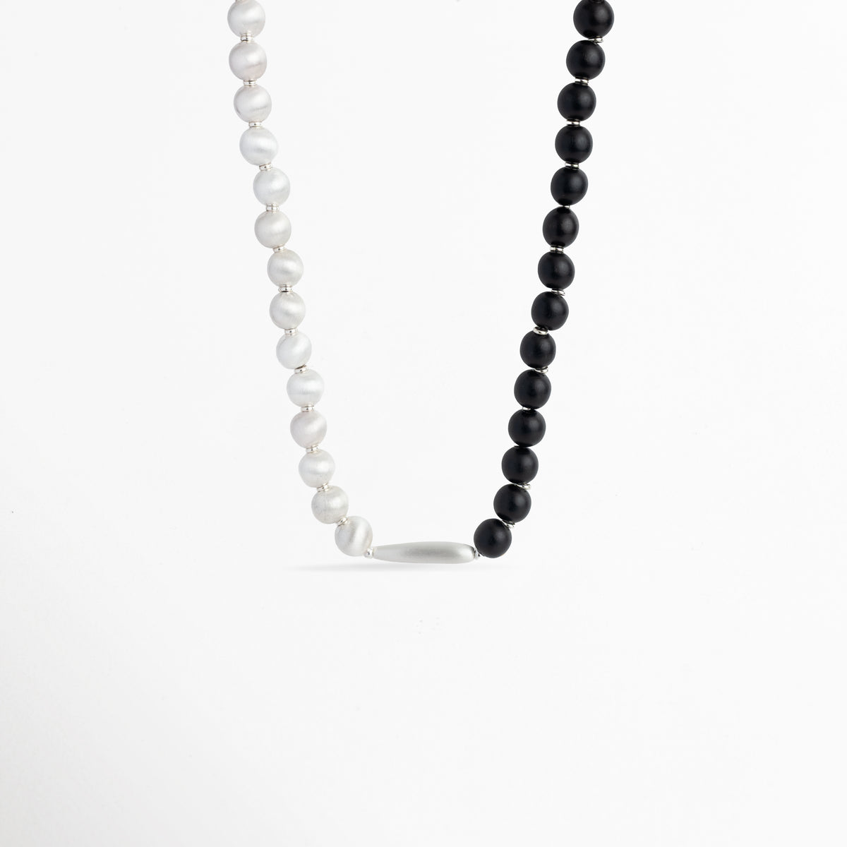 Collar Black & White con diseño divido entre esferas de madera de ébano negra y perlas blancas, unido por una barrita metálica central, vista de frente sobre fondo blanco, Vista de frente de collar duotono de 40 cm de largo y 1 cm de ancho, combinando cuentas negras mate de ébano sintético y cuentas perla satinadas, Plano general de collar bicolor de estilo orgánico y contemporáneo con conector metálico en la base sobre fondo neutro, Collar Black & White destacando 