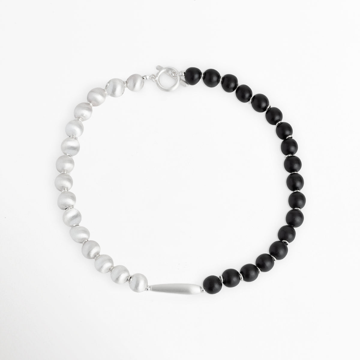Vista aérea en silueta circular del Collar Black & White mostrando la simetría dividida entre la mitad de esferas negras y la mitad perlada, Collar corto de 40 cm dispuesto en círculo perfecto resaltando la unión de madera de ébano sintética y cuentas satinadas con broche posterior, Plano general aéreo del Collar Black & White extendido sobre fondo blanco para apreciar su diseño duotono, Muestra de la distribución equilibrada de materiales