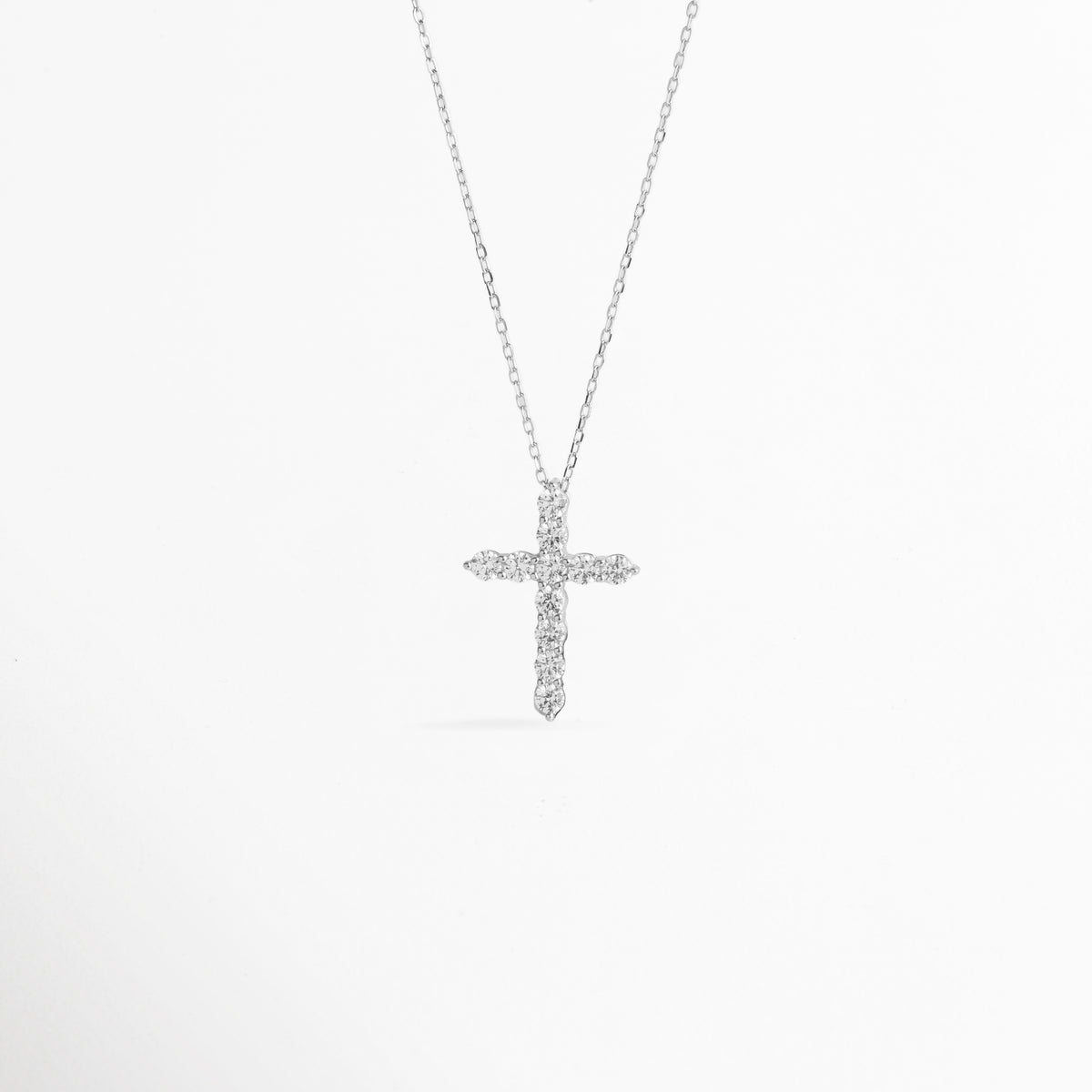 Collar Cruz Eden de plata ley 925 enchapado en oro blanco con dije de cruz latina totalmente cuajado de circonias transparentes, vista de frente sobre fondo blanco, Vista frontal de collar plateado con dije de cruz de 2.5 cm de alto enriquecido con incrustaciones de pedrería brillante, Plano general de collar fino de plata ley 925 enchapado en oro blanco con dije de cruz estilizada sobre cadena de 40 cm, Collar Cruz Eden destacando el resplandor