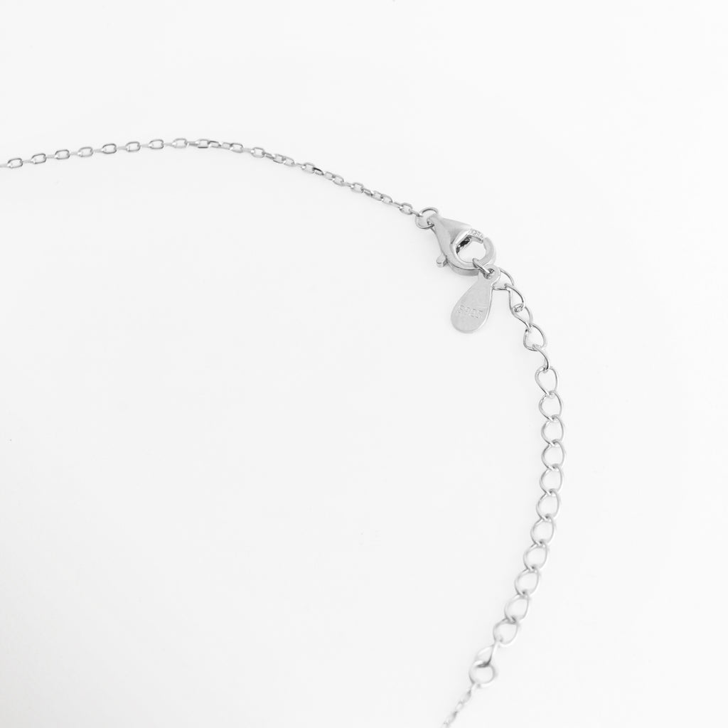 Acercamiento al broche de reasa/mosquetón y la cadena de extensión de 6 cm en la fina cadena de Plata Ley 925 del Collar Cruz Eden, Vista macro del sistema de sujeción ajustable con la medallón de marca sobre fondo blanco, Detalle de los eslabones de extensión que permiten adaptar la cadena de 40 cm a 46 cm de longitud total, Muestra del mecanismo de cierre metálico seguro y pulido en acabado de oro blanco de alta durabilidad.