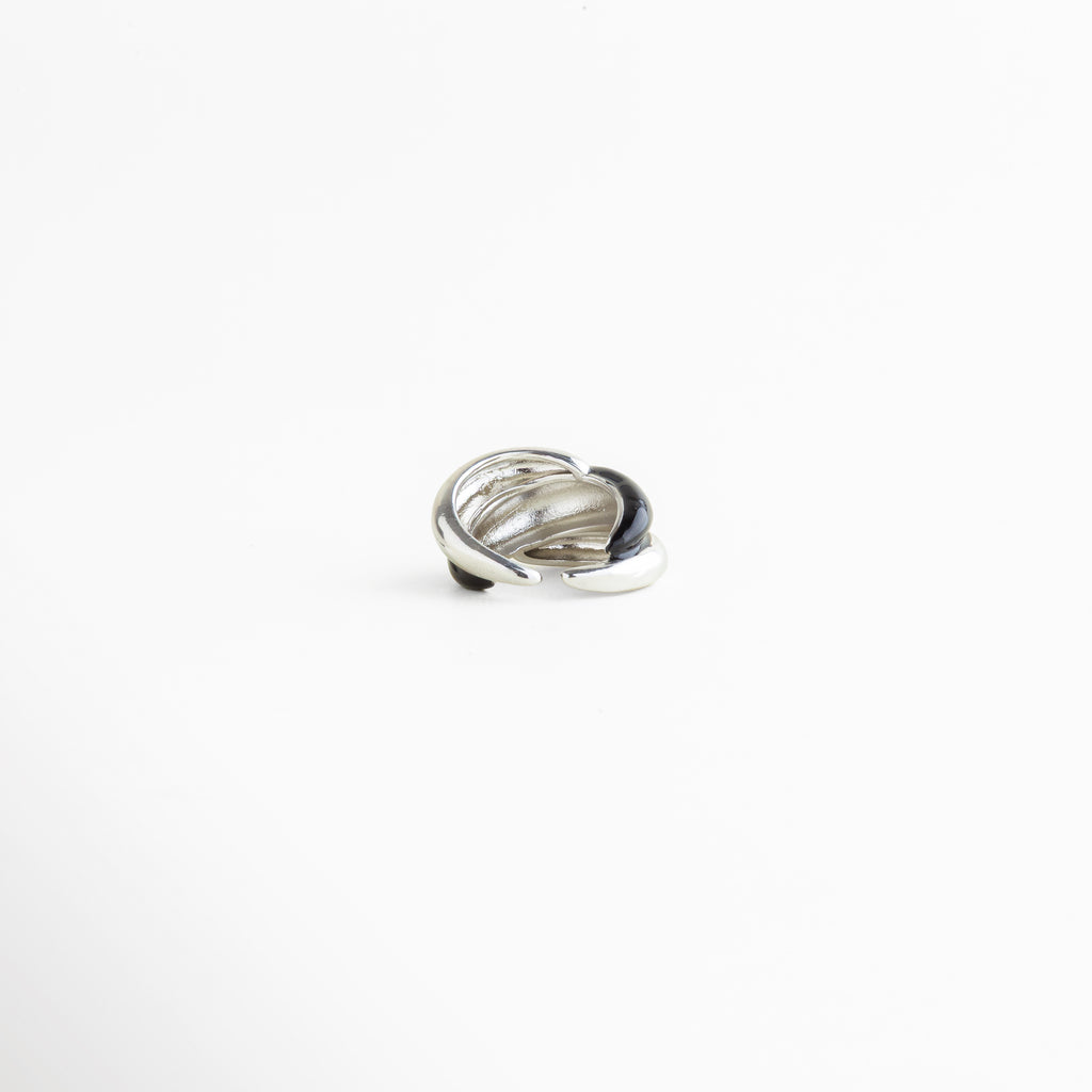 Detalle del Anillo Nerisse con acabado brillante y diseño orgánico refinado, Close up de anillo plateado con forma escultórica y estilo moderno, Detalle del recubrimiento en Oro Blanco del Anillo Nerisse, Acercamiento de anillo femenino con superficie lisa y acabado elegante, Detalle de anillo statement con contraste audaz y textura pulida.