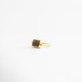 Anillo rectangular de cobre con baño de oro 18K y piedra café natural en ángulo de tres cuartos, Joyas minimalistas: anillo dorado con dije rectangular color tabaco sobre fondo blanco neutro, Detalle de anillo de sello moderno con acabado en oro 18K y piedra semipreciosa rectangular, Accesorio de bisutería fina: anillo con banda delgada dorada y piedra central café veteada, Vista lateral angular de anillo rectangular estilo Malaya Jewelry con recubrimiento de oro premium.