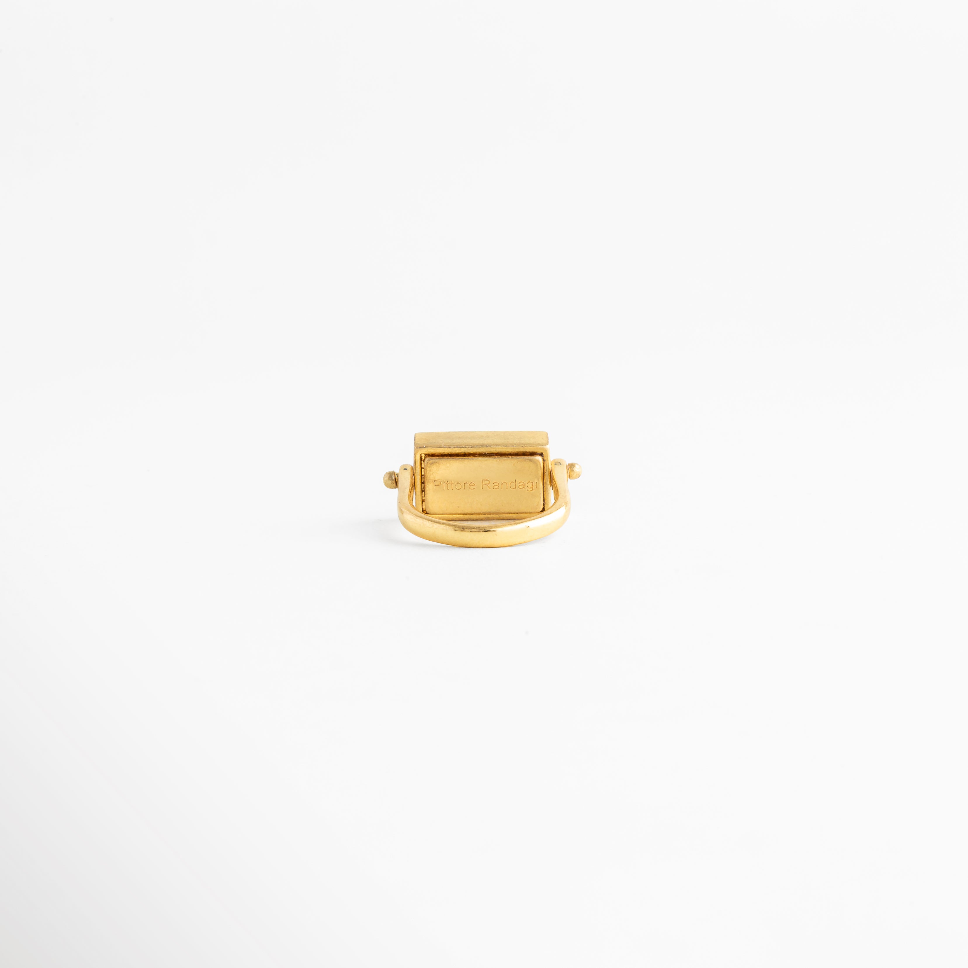 Vista trasera del anillo rectangular dorado mostrando el acabado interno y la unión de la banda, Detalle del reverso de la montura de piedra natural en anillo con baño de oro 18K, Parte interna de anillo de cobre enchapado en oro resaltando el trabajo de pulido artesanal, Perspectiva posterior de anillo minimalista que muestra la estabilidad del dije rectangular, Acabado interior de joya fina: anillo dorado con piedra café visto desde la base de la banda.
