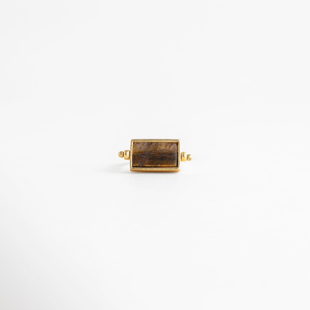 Vista frontal de anillo rectangular dorado con piedra ojo de tigre y montura de precisión, Anillo de diseño geométrico con piedra natural café en posición horizontal y acabado espejo, Top view de anillo minimalista enchapado en oro 18K con gema rectangular color tierra, Simetría perfecta: anillo dorado con piedra café central para catálogo de joyería de lujo, Detalle de la cara principal del anillo rectangular con bordes definidos y baño de oro.