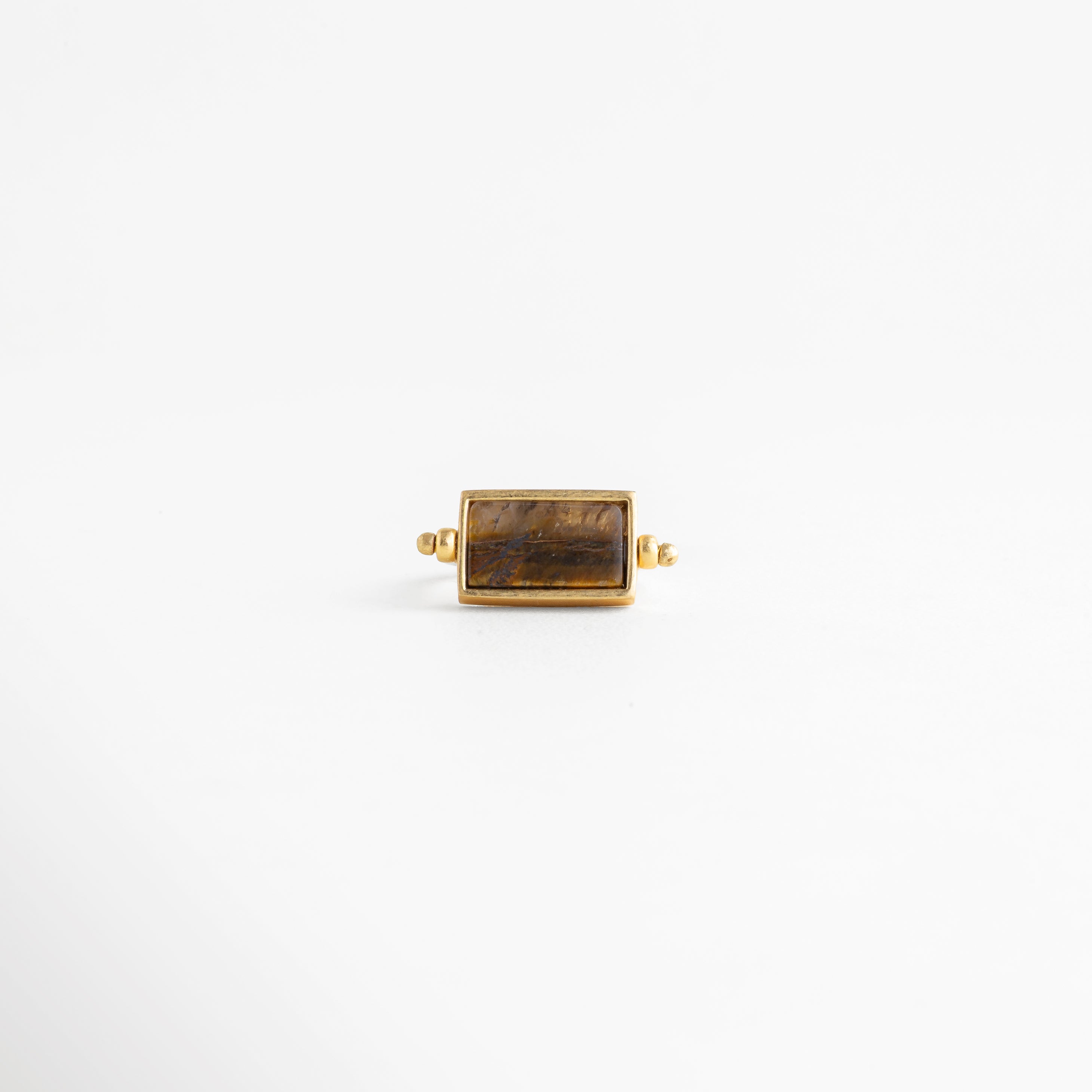 Vista frontal de anillo rectangular dorado con piedra ojo de tigre y montura de precisión, Anillo de diseño geométrico con piedra natural café en posición horizontal y acabado espejo, Top view de anillo minimalista enchapado en oro 18K con gema rectangular color tierra, Simetría perfecta: anillo dorado con piedra café central para catálogo de joyería de lujo, Detalle de la cara principal del anillo rectangular con bordes definidos y baño de oro.