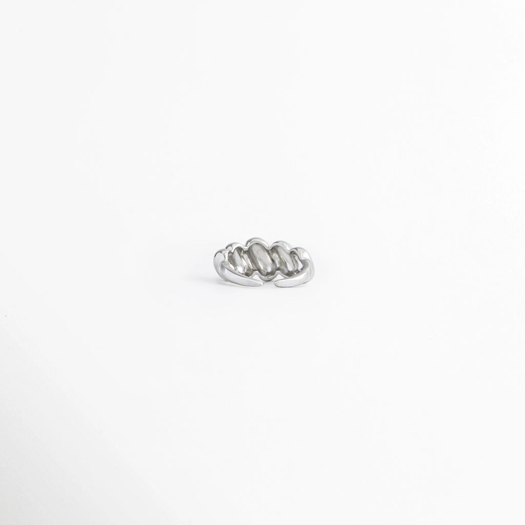 Vista superior del Anillo Virella destacando el diseño entrelazado de bandas metálicas, Anillo Virella visto desde arriba mostrando su estructura de líneas curvas y acabado brillante, Detalle superior del Anillo Virella con diseño geométrico de inspiración retro, Vista aérea del Anillo Virella con acabado pulido y diseño entrelazado, Anillo Virella con diseño de bandas cruzadas visto desde la parte superior.