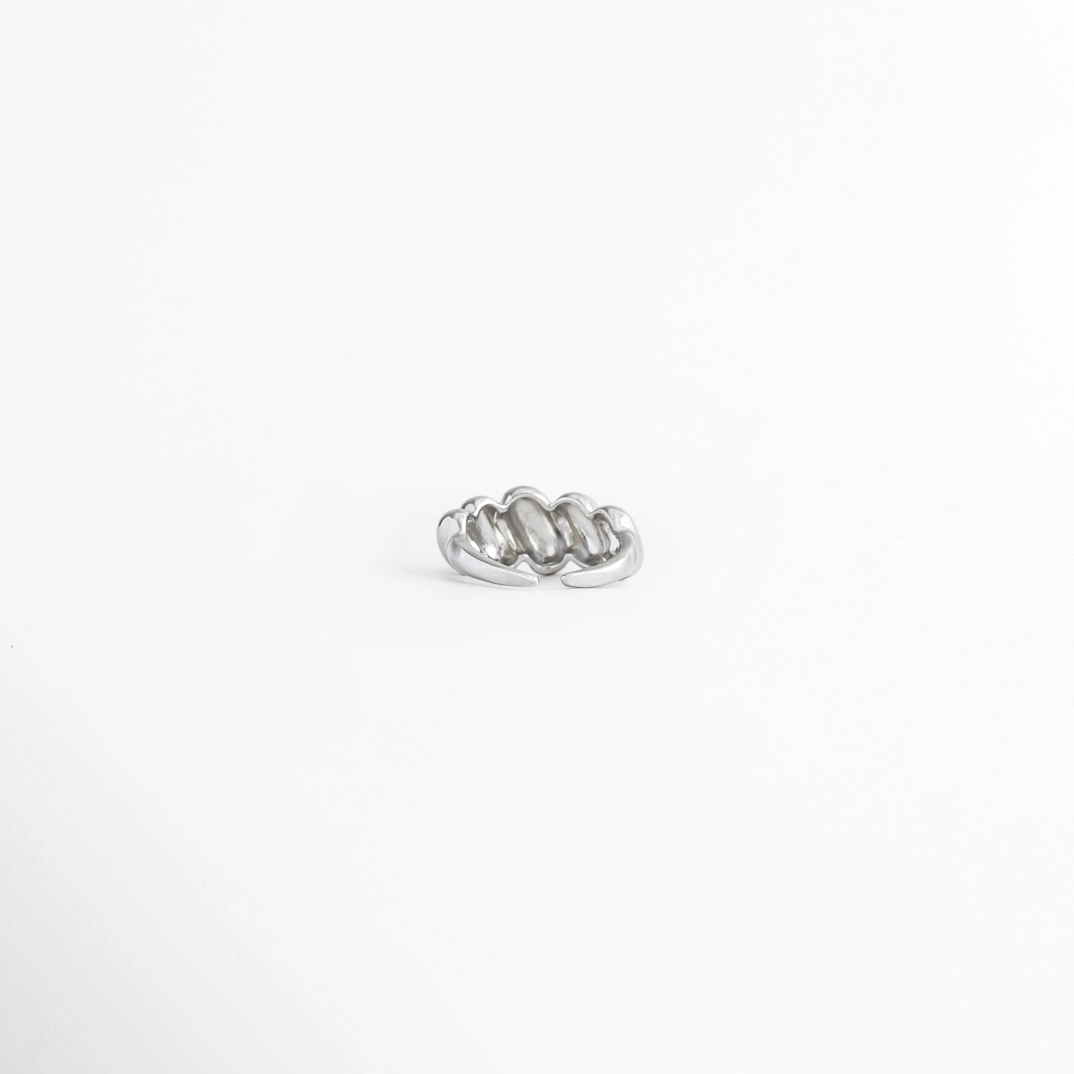 Vista superior del Anillo Virella destacando el diseño entrelazado de bandas metálicas, Anillo Virella visto desde arriba mostrando su estructura de líneas curvas y acabado brillante, Detalle superior del Anillo Virella con diseño geométrico de inspiración retro, Vista aérea del Anillo Virella con acabado pulido y diseño entrelazado, Anillo Virella con diseño de bandas cruzadas visto desde la parte superior.