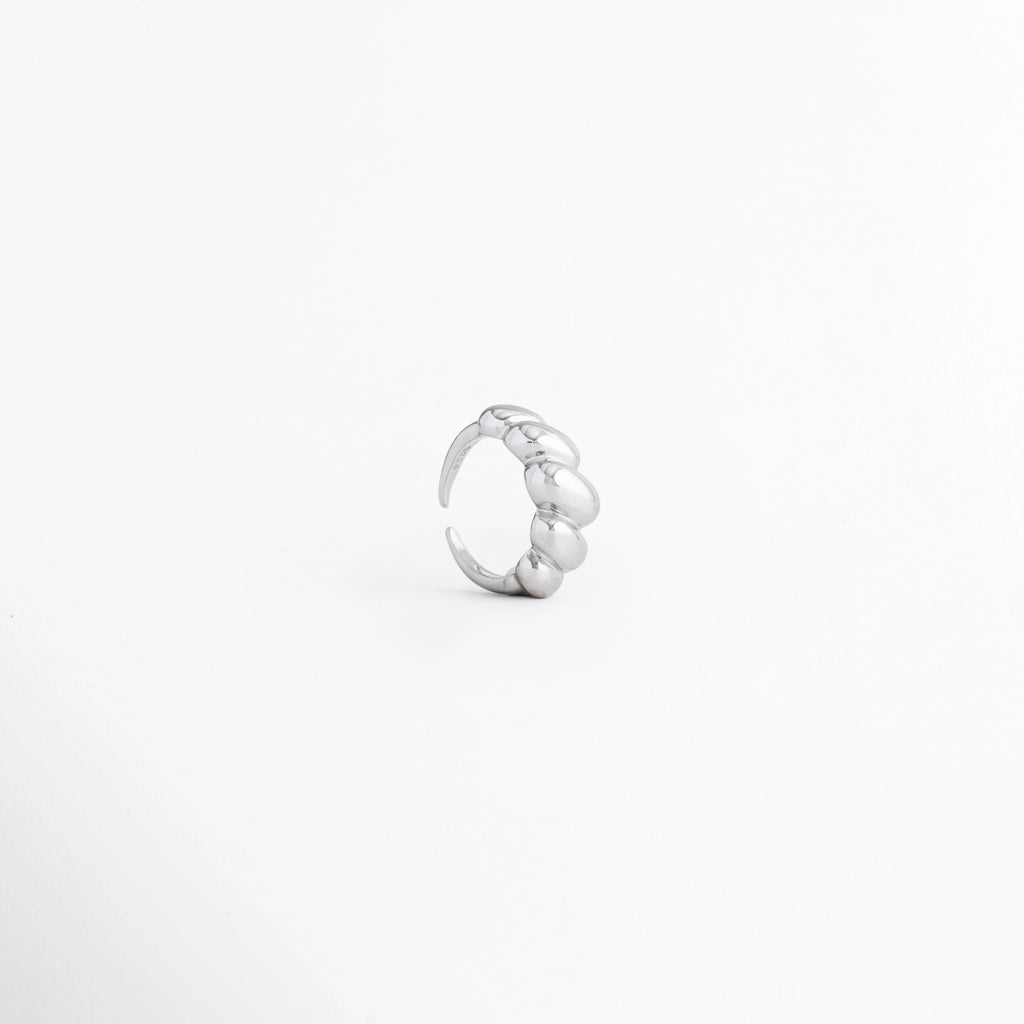 Vista lateral del Anillo Virella mostrando su diseño ajustable y acabado plateado brillante, Perfil del Anillo Virella con estructura abierta y diseño entrelazado, Anillo Virella en vista de costado destacando su ajuste abierto y líneas curvas, Detalle lateral del Anillo Virella elaborado en cobre con acabado pulido brillante, Vista de perfil del Anillo Virella mostrando el diseño ajustable y el interior del anillo.
