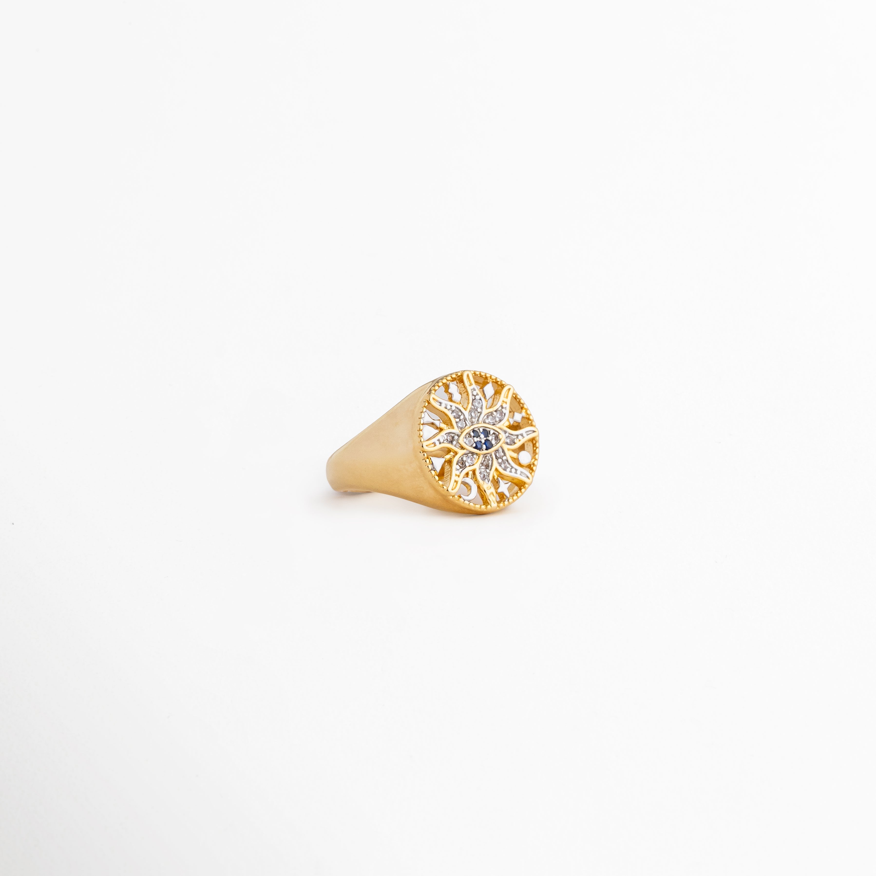 Vista lateral inclinada del anillo Alaric mostrando el relieve de la corona redonda, Detalle del acabado pulido en oro de 14K y la forma cónica del anillo tipo sello, Anillo dorado brillante expuesto en ángulo sobre fondo claro neutro, Enfoque del diseño místico con zirconias capturando la luz de lado, Perspectiva de catálogo del anillo de sol calado chapado en oro.