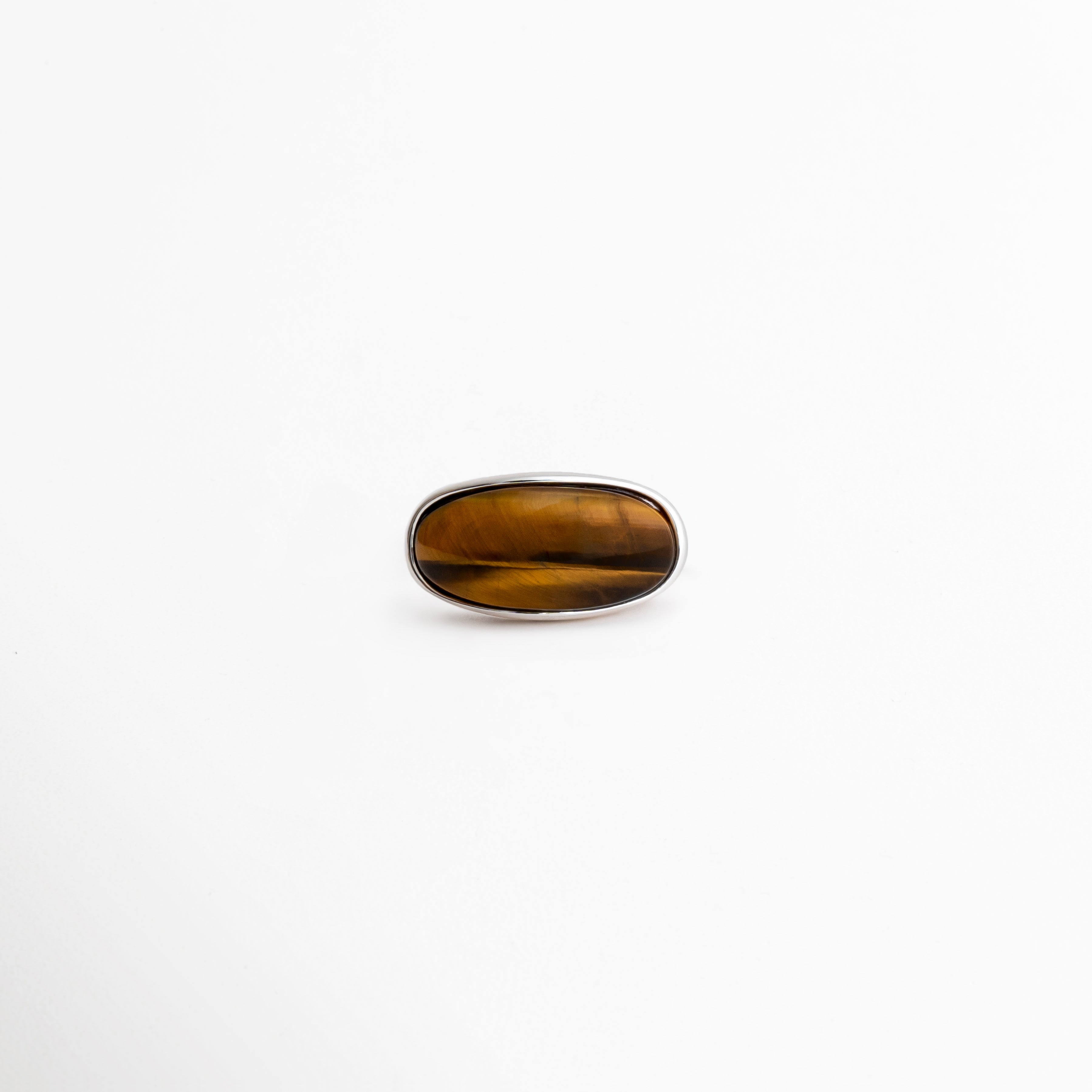 Primer plano de la piedra Ojo de Tigre mostrando sus vetas naturales marrones y doradas, Detalle de la gema ovalada con acabado brillante tipo cabujón del anillo Kaio, Vista superior del anillo destacando el patrón único de la piedra Ojo de Tigre, Textura lisa y reflejos naturales de la piedra semipreciosa del anillo, Gema Ojo de Tigre de corte alargado engastada en acabado oro blanco.