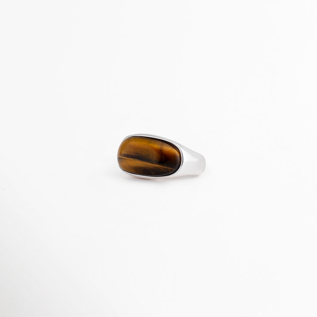 Anillo Kaio plateado con piedra natural Ojo de Tigre de corte ovalado, Anillo ajustable chapado en oro blanco con gema Ojo de Tigre lisa, Joyería moderna para mujer: anillo grueso de oro blanco y piedra marrón, Vista de tres cuartos del anillo ajustable Kaio sobre fondo blanco limpio, Anillo de cobre con enchapado plateado y piedra central protectora Ojo de Tigre.