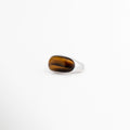 Anillo Kaio plateado con piedra natural Ojo de Tigre de corte ovalado, Anillo ajustable chapado en oro blanco con gema Ojo de Tigre lisa, Joyería moderna para mujer: anillo grueso de oro blanco y piedra marrón, Vista de tres cuartos del anillo ajustable Kaio sobre fondo blanco limpio, Anillo de cobre con enchapado plateado y piedra central protectora Ojo de Tigre.