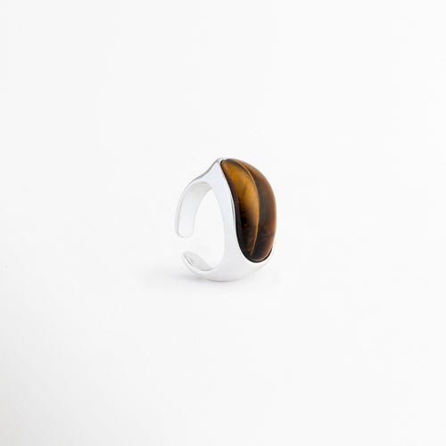 Vista lateral del anillo Kaio mostrando el grosor de la banda de oro blanco, Perfil de anillo minimalista plateado con montura integrada de piedra natural, Detalle del acabado pulido en oro blanco y la curvatura de la gema, Estructura de anillo chunky chapado en oro blanco con piedra Ojo de Tigre, Enfoque de perfil de la montura lisa del anillo de cobre plateado.