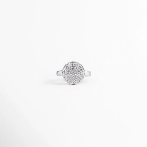 Anillo ajustable de enchapado en oro blanco con dije circular plano totalmente cubierto de pavé de circonias, vista frontal sobre fondo blanco, Detalle superior de anillo con medallón redondo cuajado de circonias brillantes en acabado plateado, Anillo ajustable de plata/oro blanco con centro circular de micropavé deslumbrante en toma frontal, Anillo de bisutería fina ajustable con gran círculo central de incrustaciones de piedras circonias.
