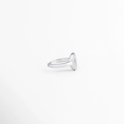 Vista de perfil de anillo ajustable mostrando el grosor de la placa circular superior y el aro plateado pulido, Ángulo lateral de anillo enchapado en oro blanco que muestra la elevación del medallón con circonias, Perspectiva de tres cuartos de anillo con dije redondo brillante y estructura estilizada, Detalle lateral de la base de cobre con baño de oro blanco y cabeza circular incrustada, Anillo con medallón de circonias visto desde el costado sobre fondo blanco.