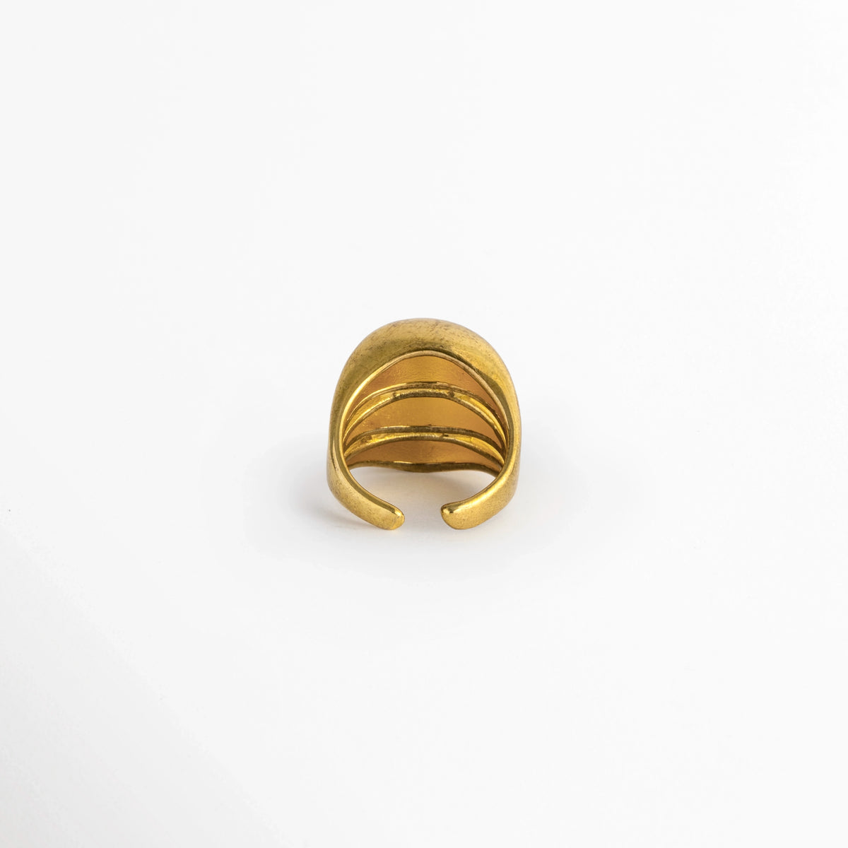  Vista de la cara posterior del Anillo Cass mostrando la abertura inferior ajustable que permite graduar el tamaño, Acercamiento al reverso del anillo dorado abierto con bordes redondeados y suaves para un ajuste cómodo, Toma posterior que muestra la cavidad interna pulida y el sistema adaptable del anillo,  Muestra de la flexibilidad de la caña de cobre enchapada en oro para adaptarse a distintas medidas de dedo. 