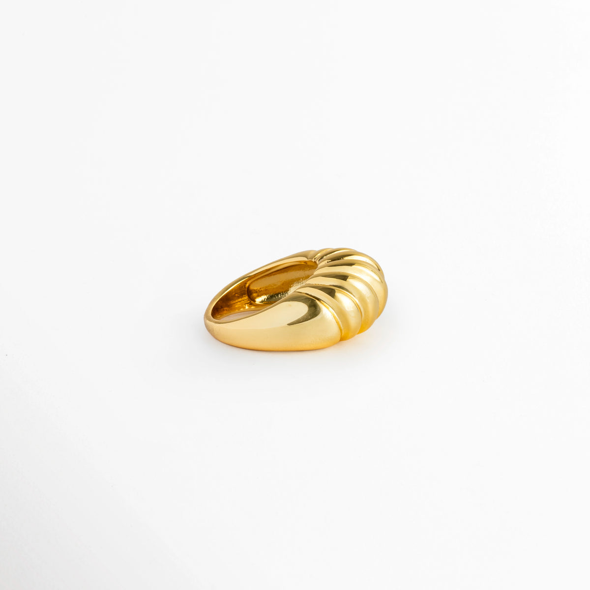 Anillo Bolt Golden visto de perfil acostado sobre fondo blanco, mostrando la curva abombada y el volumen de su diseño, Vista lateral de anillo abultado dorado exhibiendo la elevación del domo acanalado, Detalle de perfil de la silueta en domo del anillo con acanalado horizontal en acabado brillante, Perspectiva lateral de anillo chunky dorado reposando en superficie neutra.
