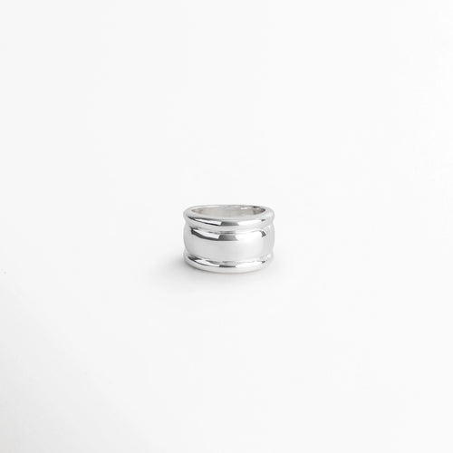Anillo Tamara ancho de acero inoxidable con silueta cóncava y bordes redondeados en acabado plateado, vista frontal sobre fondo blanco, Anillo de banda ancha de 1.3 cm con diseño abombado y pulido espejo brillante en color plata, Vista de frente de anillo plateado de silueta fluida con cuerpo cóncavo y curvatura suave, Anillo grueso de acero con recubrimiento PVD en tono plata brillante sobre superficie neutra.
