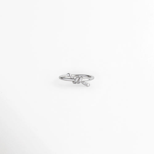 Anillo Node enchapado en oro blanco de 18K con motivo central de nudo estilizado e incrustaciones de circonia, vista frontal sobre fondo blanco, Anillo delgado plateado con detalle de nudo orgánico decorado con microcirconias en el centro, Vista de frente de anillo de promesa con diseño de nudo entrelazado en tono plata y pedrería brillante, Anillo fino de latón con recubrimiento en oro blanco 18K y nudo de 0.5 cm con circonias engastadas.