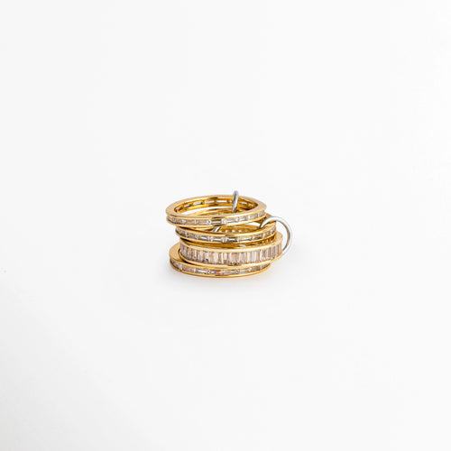 Anillo Leonora multiaro de tono oro 18K con hileras de circonias incrustadas, compuesto por aros finos unidos en conjunto sobre fondo blanco, Anillo apilado de varios aros dorados delgados con incrustaciones de pedrería y conector metálico, Vista de frente de anillo churumbela múltiple entrelazada enchapada en oro 18K con circonias brillantes, Anillo grueso de aros múltiples superpuestos en tono oro cálido con diminutas circonias pavé.