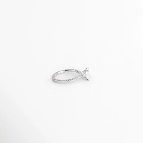 Anillo de compromiso visto de perfil acostado sobre fondo blanco, mostrando la silueta delgada de la banda y el engaste elevado de la piedra, Vista lateral plana de solitario de plata enchapado en oro blanco exhibiendo el perfil bajo del engaste con gema rectangular, Detalle de perfil de la banda delgada del anillo con acabado pulido y elevación de la gema principal, Perspectiva lateral de anillo de promesa rectangular acostado en superficie neutra.