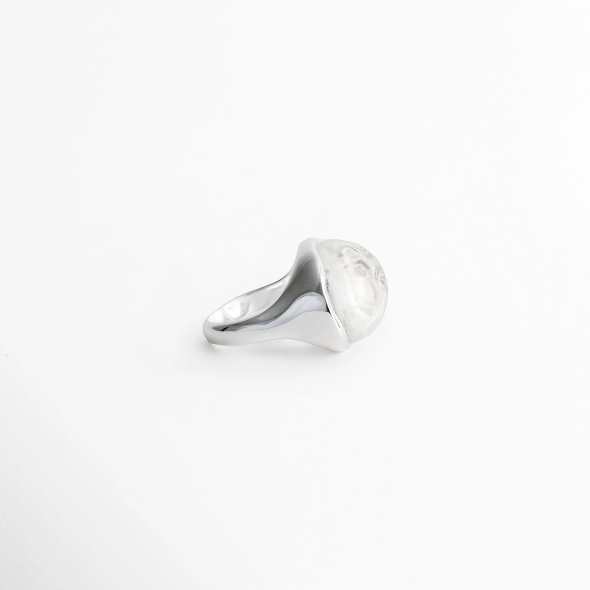Vista de perfil del Anillo Palencia mostrando la altura de la piedra cristalina abombada y el cuerpo ergonómico del anillo, Acercamiento lateral al bisel de latón enchapado en oro blanco que abraza la gema cristalina orgánica, Toma en ángulo que resalta la transición fluida entre la banda plateada pulida y el domo de cristal, Muestra de la elevación y volumen tridimensional del Anillo Palencia de 2.3 cm de ancho.