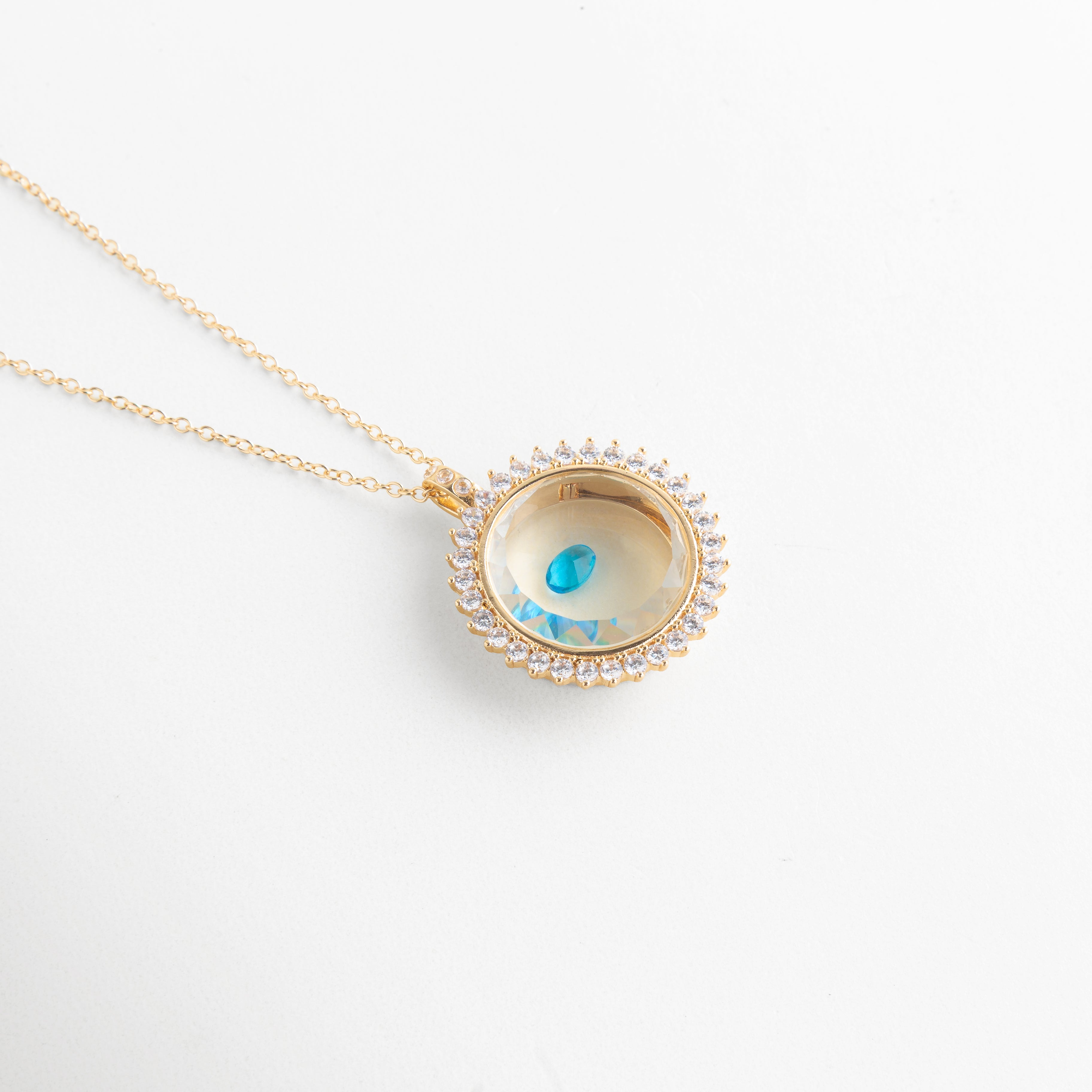 Collar dorado con dije circular y piedra de cristal celeste brillante, Dije elegante con cristal azul claro en diseño delicado, Joyería fina con piedra celeste en accesorio minimalista, Collar delicado con cristal azul cielo pequeño y brillante, Accesorio de bisutería con gema celeste en diseño moderno