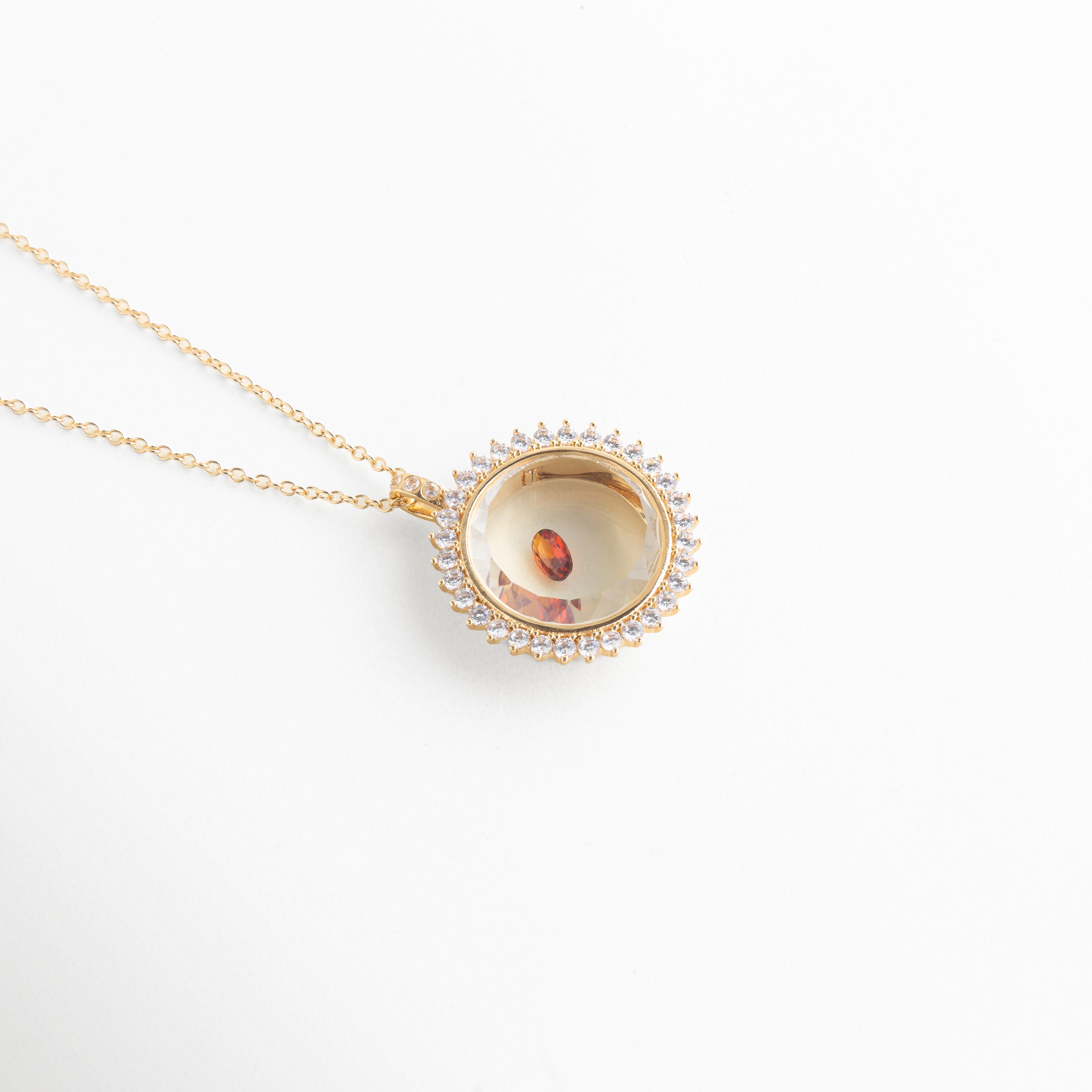 Collar dorado con dije circular y piedra de cristal color ámbar, Dije elegante con cristal central en tonos cálidos y acabado brillante, Joyería fina con piedra artificial de cristal en diseño delicado, Collar minimalista con cristal pequeño de color rojo anaranjado, Accesorio de bisutería con gema de cristal brillante en diseño moderno